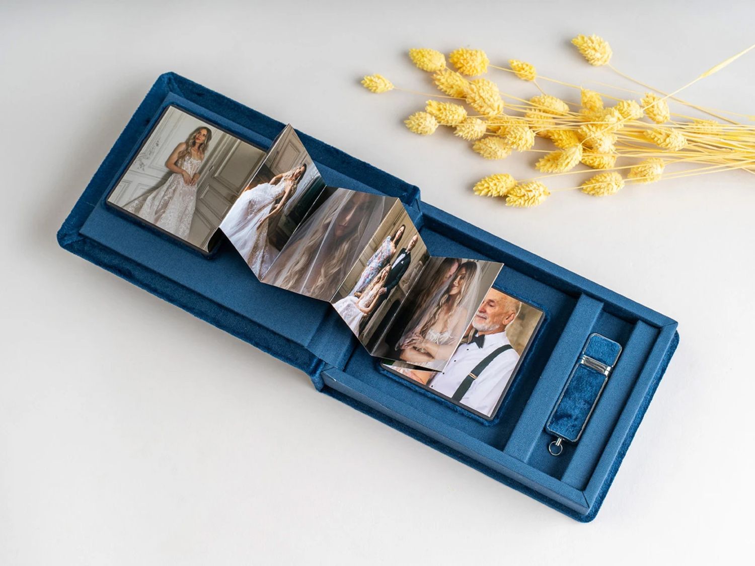 Blue photo album box open displaying wedding photos, with dried yellow flowers on white background. Northern ireland weddings