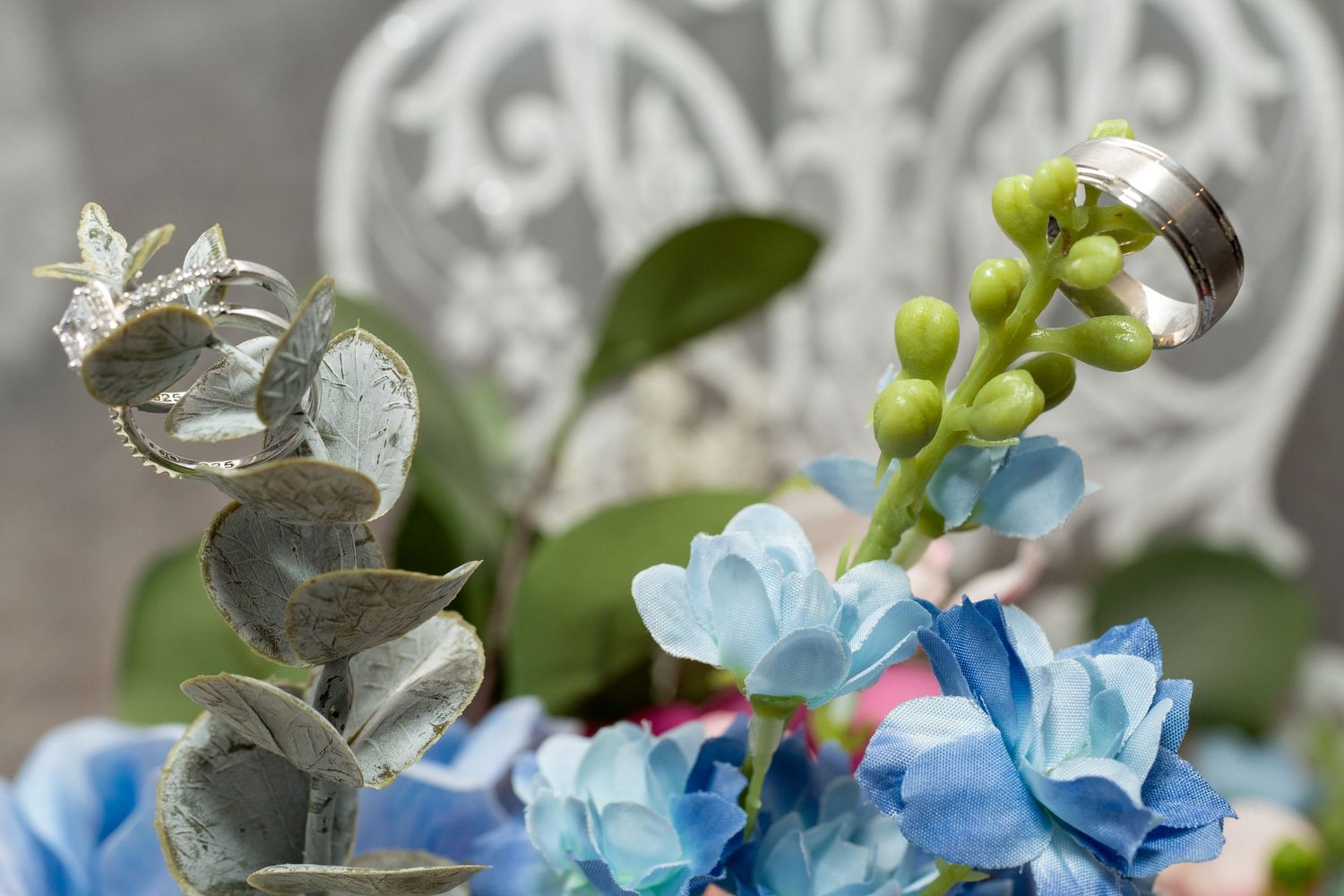 Close-up of blue hydrangeas and eucalyptus with a silver wedding band resting on green flower buds. Dave martin weddings