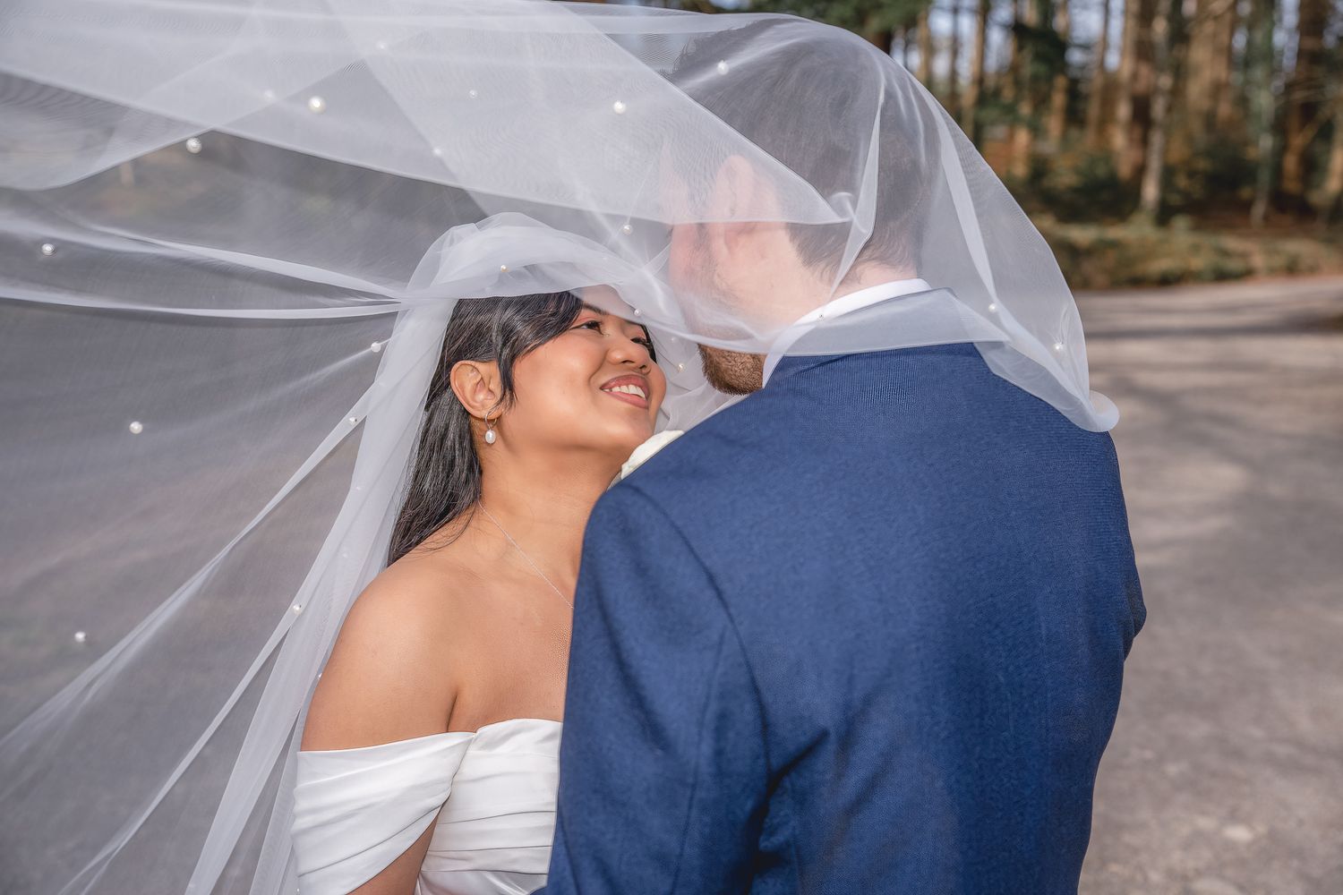 Bride and groom sharing a romantic moment under a flowing white veil outdoors on their wedding day.