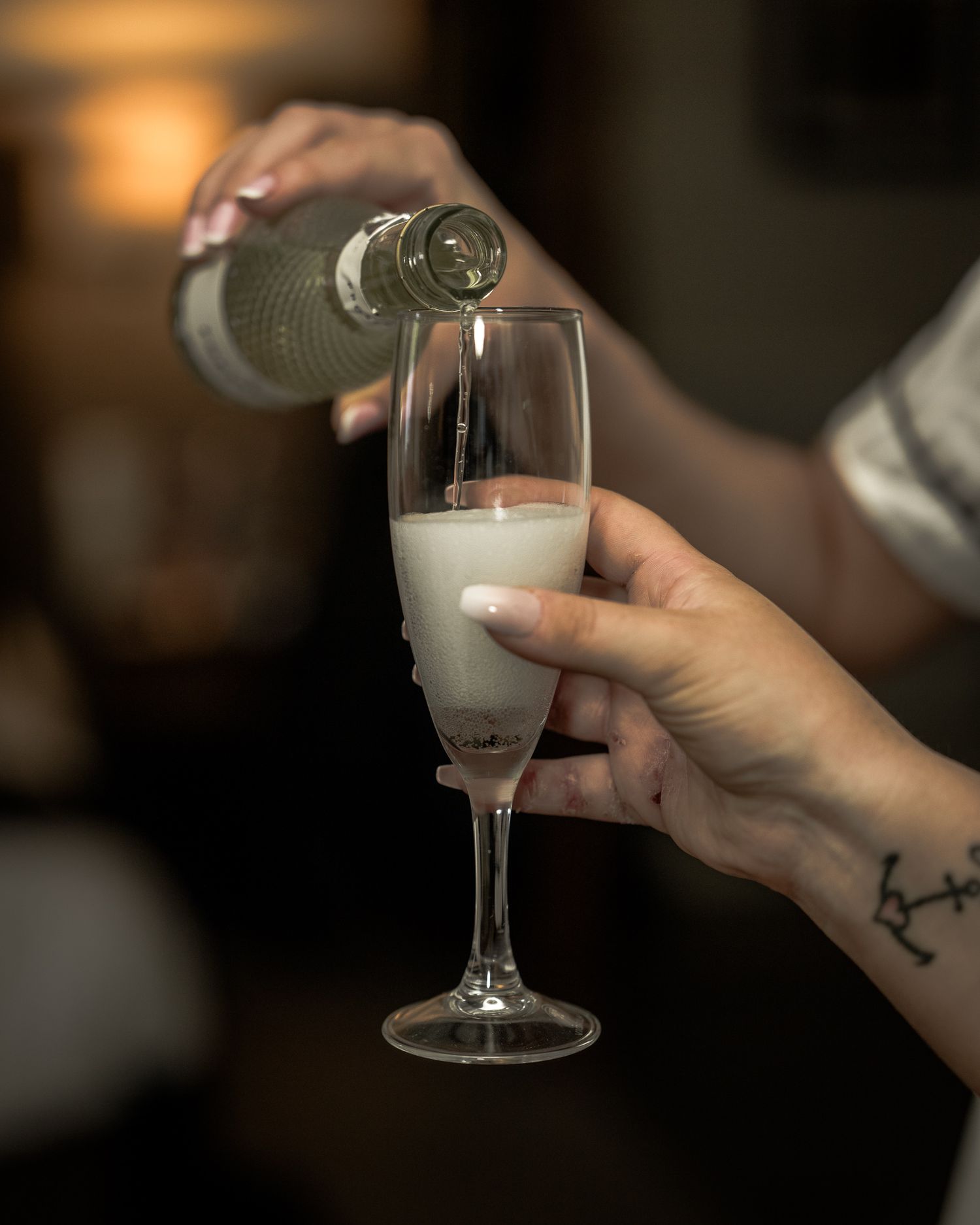 A bridesmaidpouring a creamy white cocktail into a champagne flute held by a person with a small tattoo. Dave Martin wedding Photographer NI