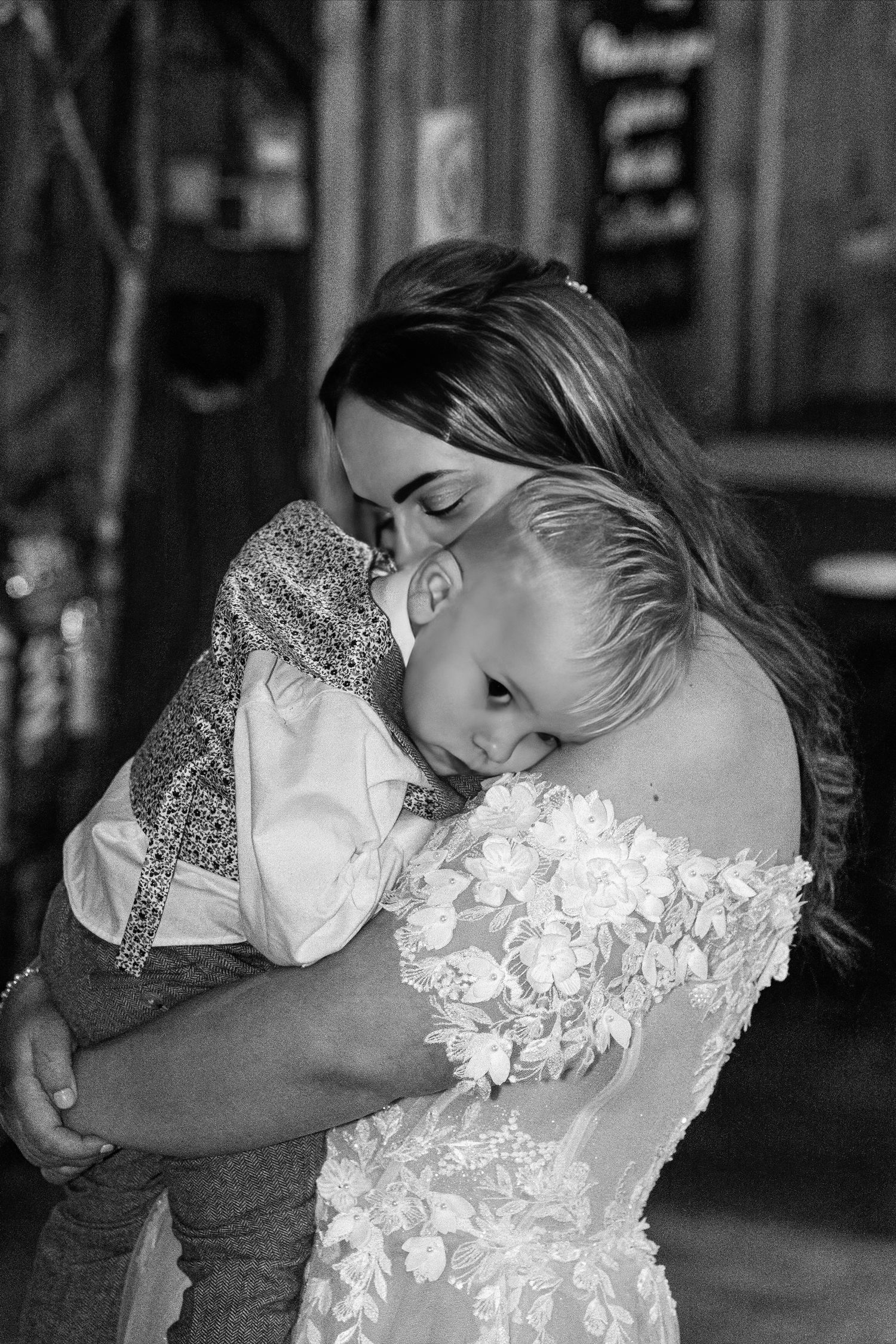 Black and white photo of bride tenderly embracing young child. Dave Martin Photographer Northern Ireland