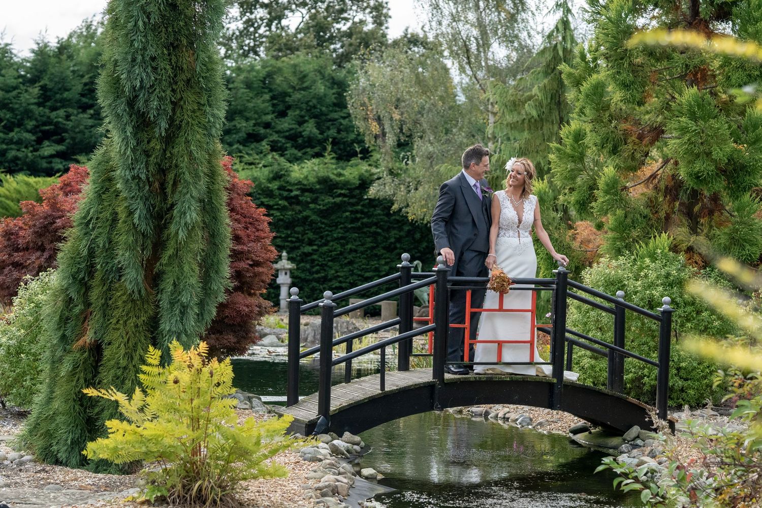 Bride and groom walking on ornamental bridge in garden. Dave Martin Photographer Northern Ireland