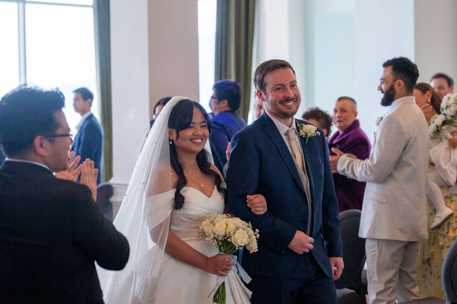 Bride and groom walking down aisle smiling after wedding ceremony, bride holding white roses bouquet. Dave Martin Photographer Northern Irel