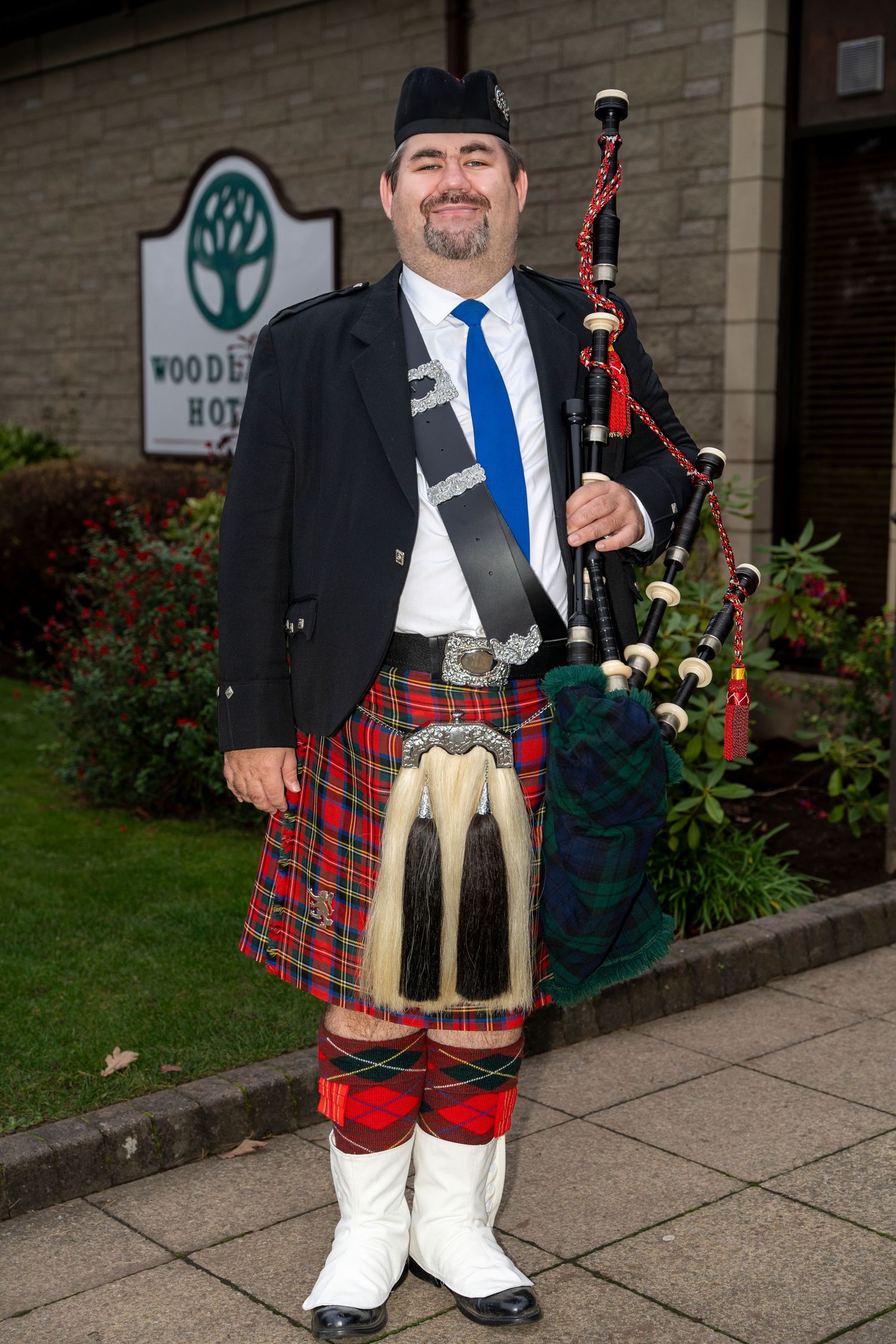 Scottish bagpiper in Royal Stewart tartan kilt performing outside Woodend Hotel. Dave Martin Photographer Northern Ireland