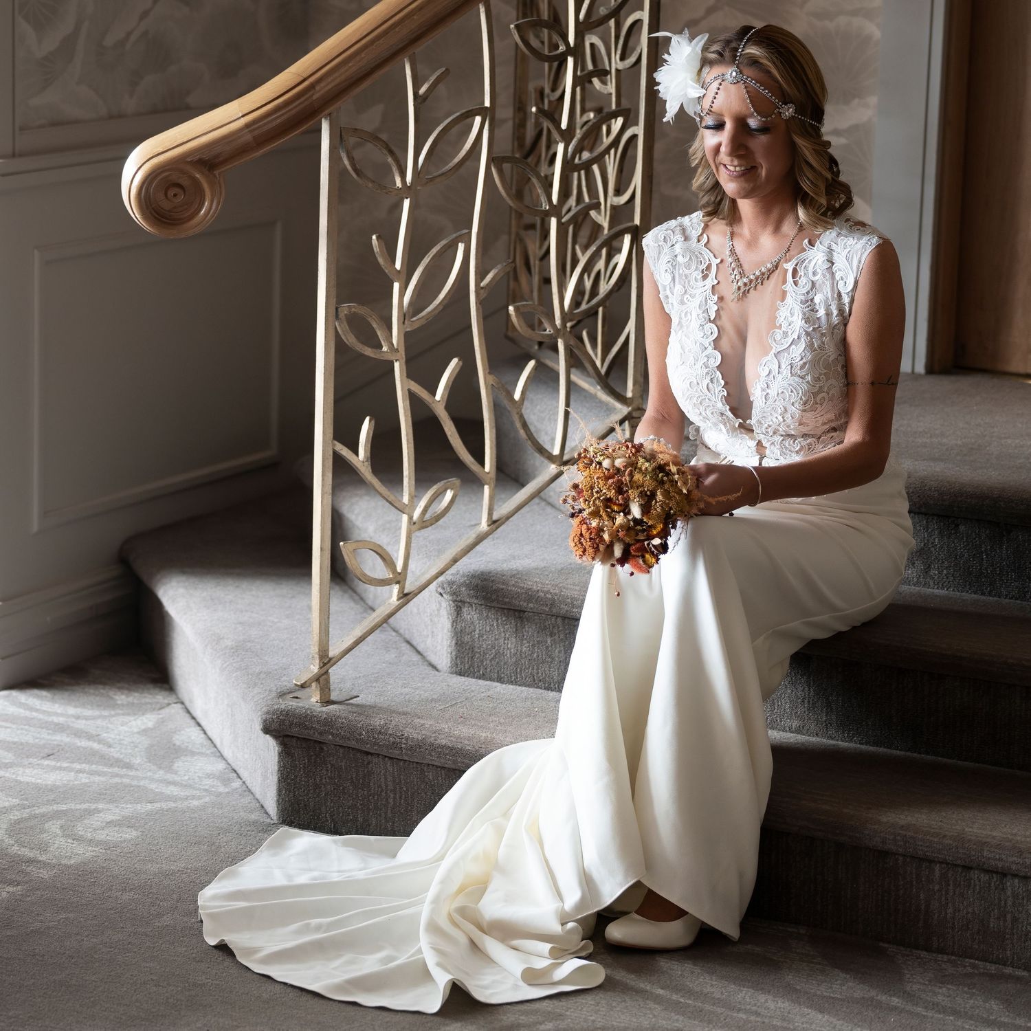 Elegant bride in white lace gown sitting on stairs holding bouquet. Dave Martin Photographer Northern Ireland