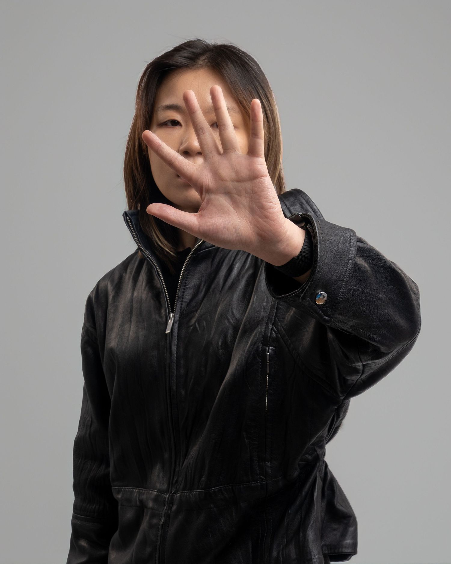 An Asian woman in a black jacket holding her palm up toward the camera in a stop gesture. Dave Martin Photography Studio Belfast