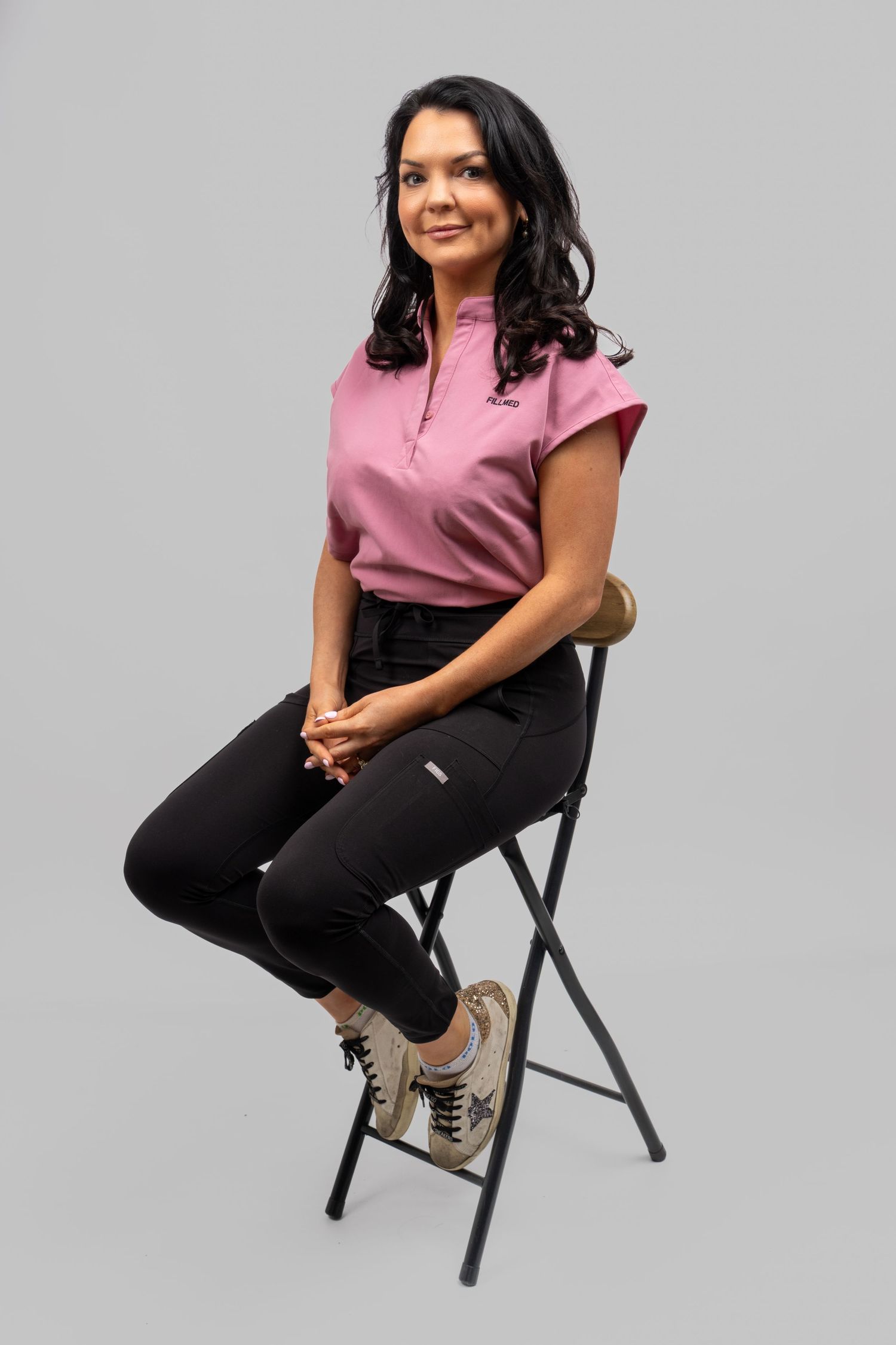 Woman in pink top and black pants sitting on folding chair in gray studio. Dave Martin Photography Studio Belfast