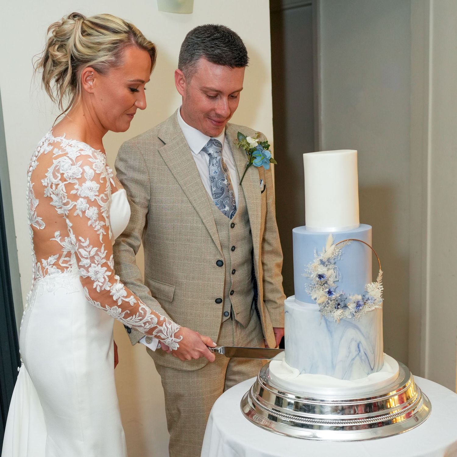 Bride and groom in elegant attire cutting a stunning three-tier marble and gold wedding cake together. Dave Martin Photographer Belfast