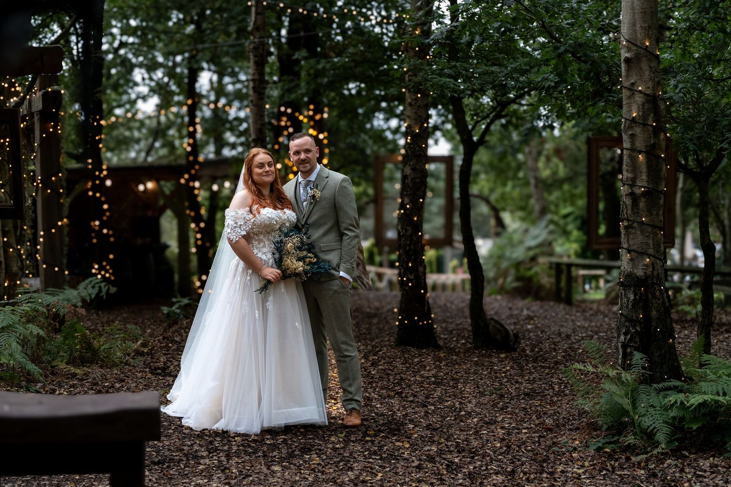 Bride in white tulle gown and groom pose among fairy-lit trees at a woodland wedding. Dave Martin Photographer Northern Ireland