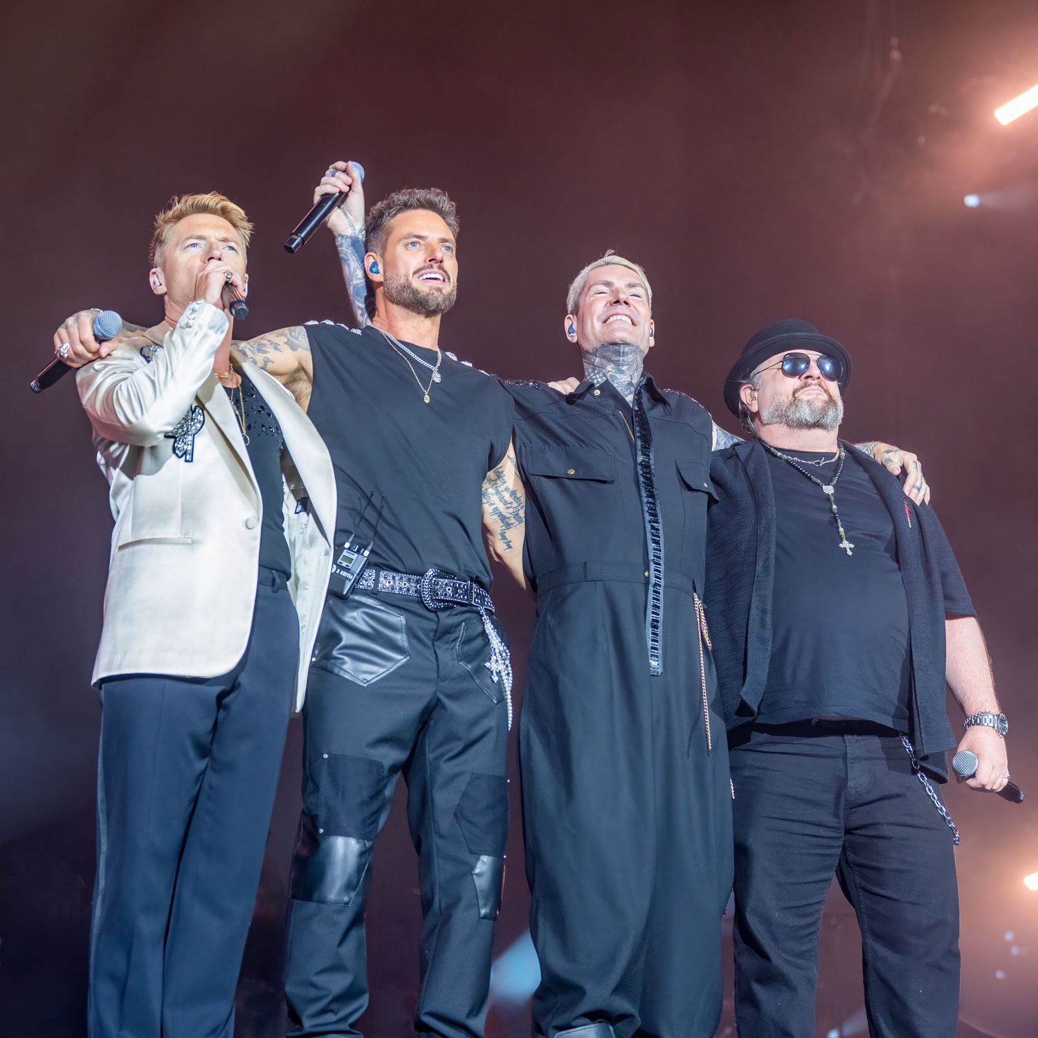 Four male performers singing on stage under bright lights during a live concert performance. Dave martin weddings