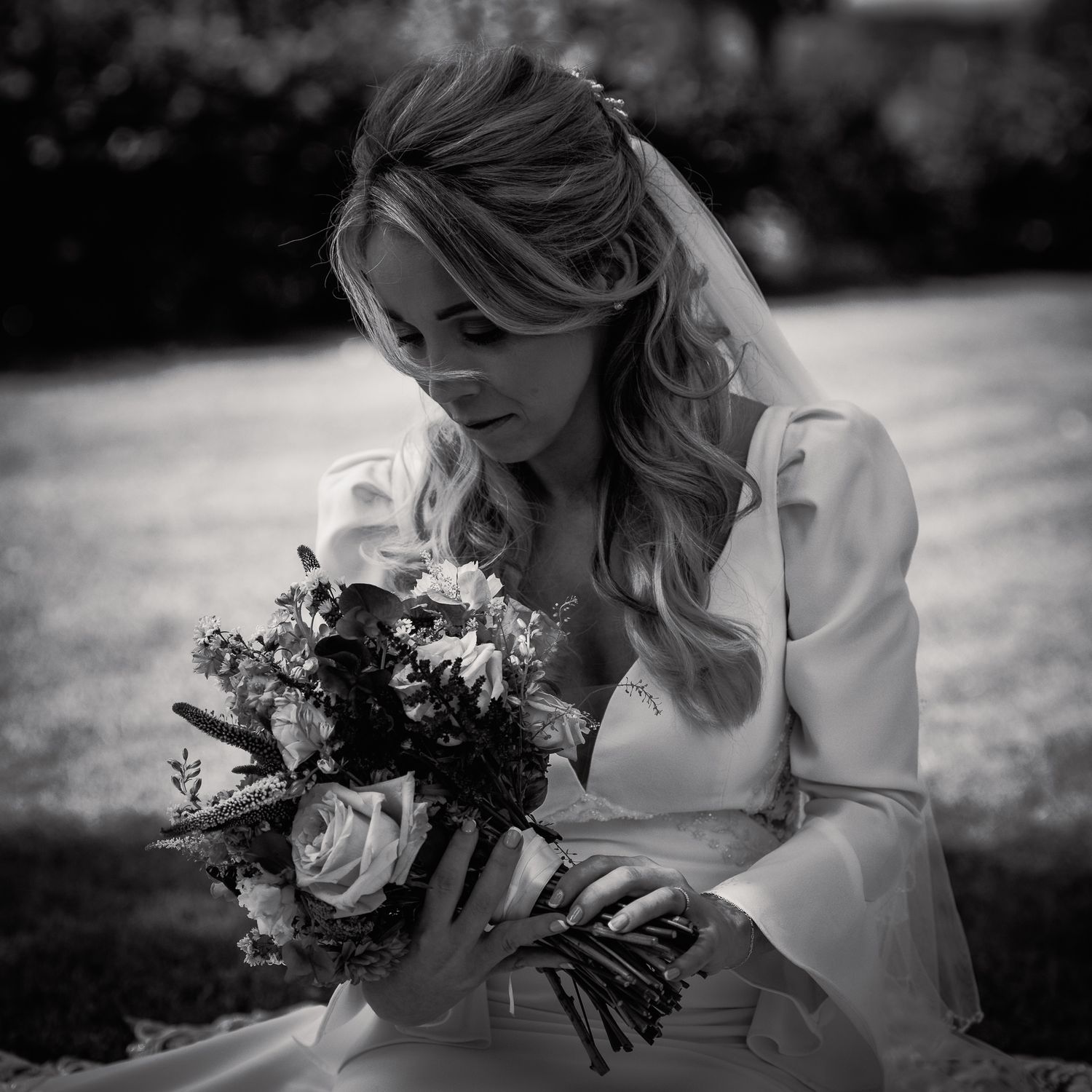 Black and white photo of a bride in a white gown holding a floral bouquet, gazing downward with soft curled hair. Roe valley resort Weddings