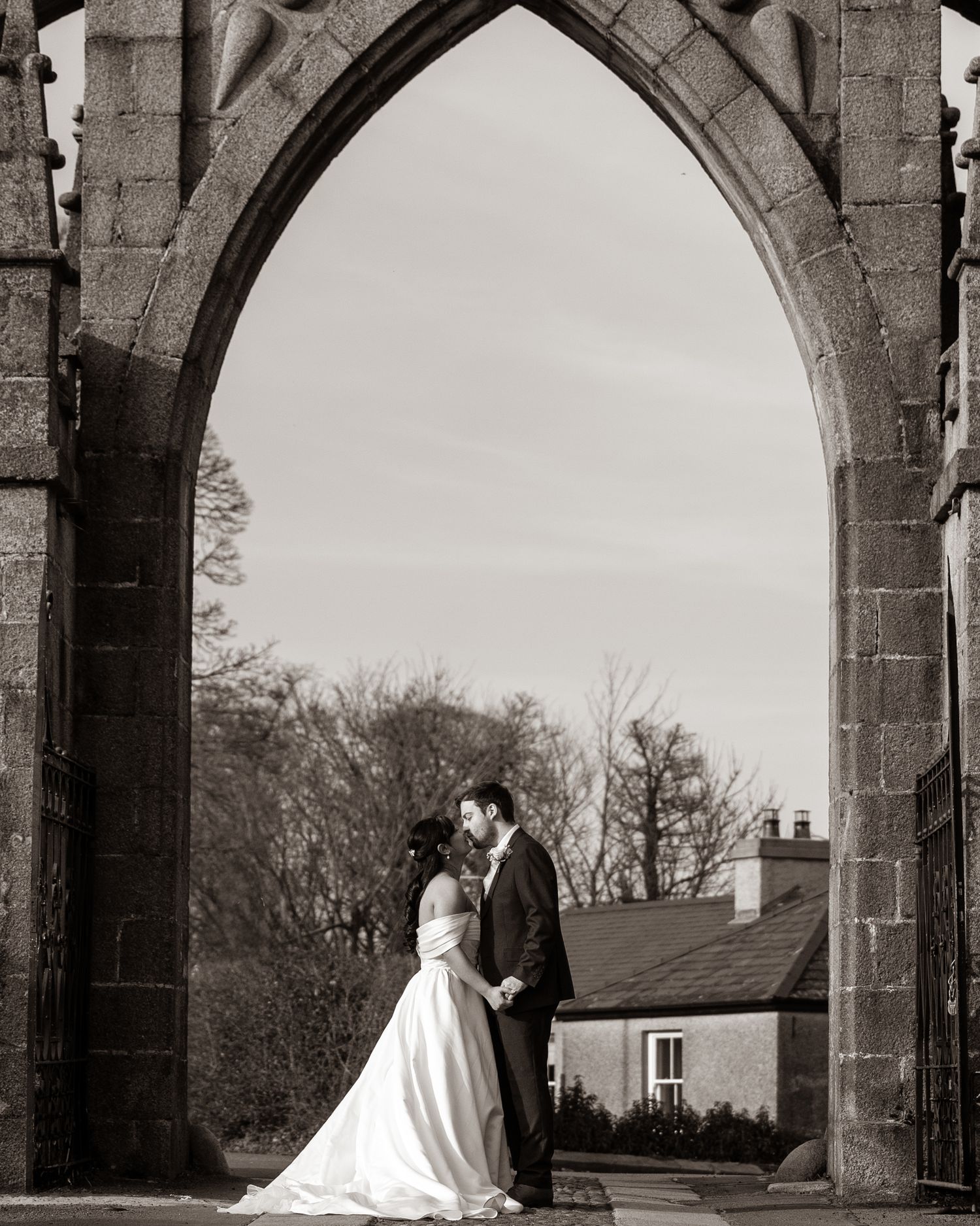 Bride and groom share romantic moment under gothic stone arch in black and white wedding portrait. Dave Martin Photographer Northern Ireland