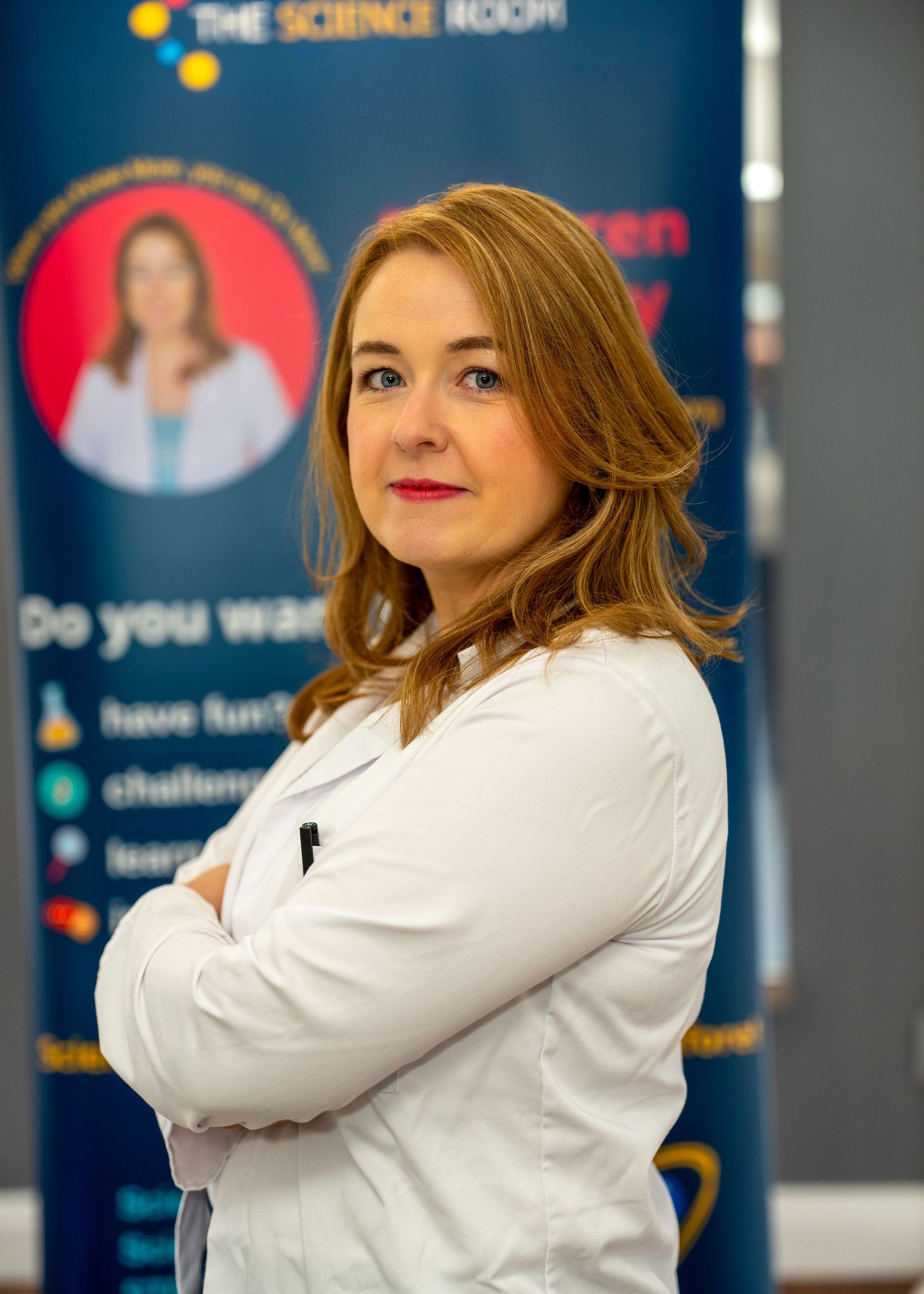 Woman in white lab coat standing with arms crossed in front of The Science Room promotional banner display. Dave Martin Photography Northern