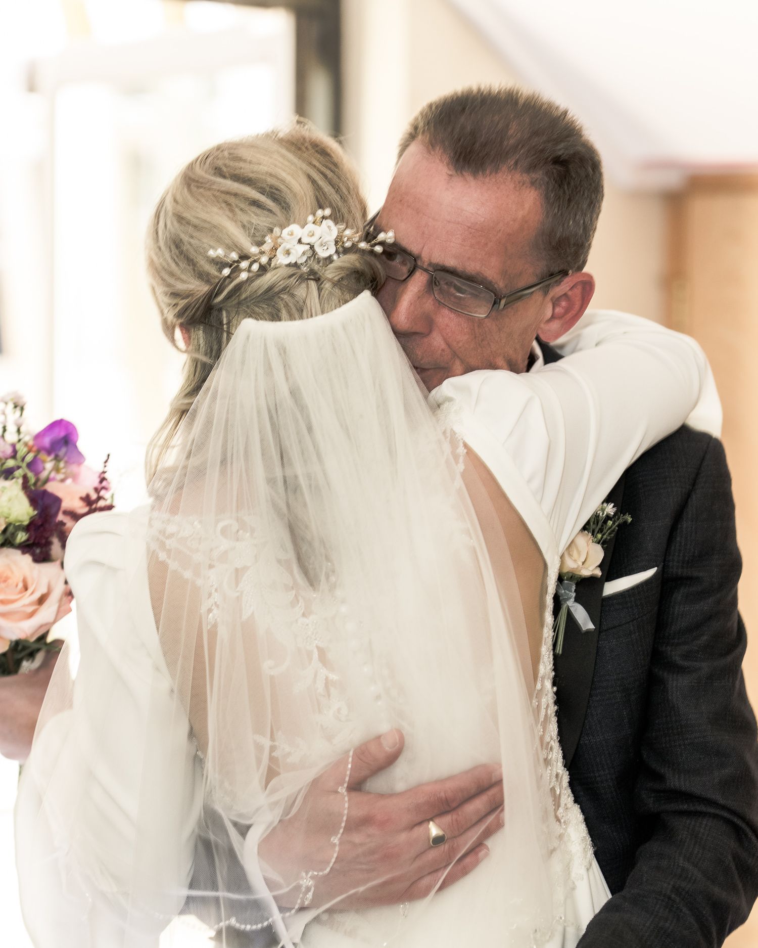 Emotional wedding moment as bride and her father share a heartfelt embrace, bride wearing veil and floral headpiece.  Dave Martin wedding