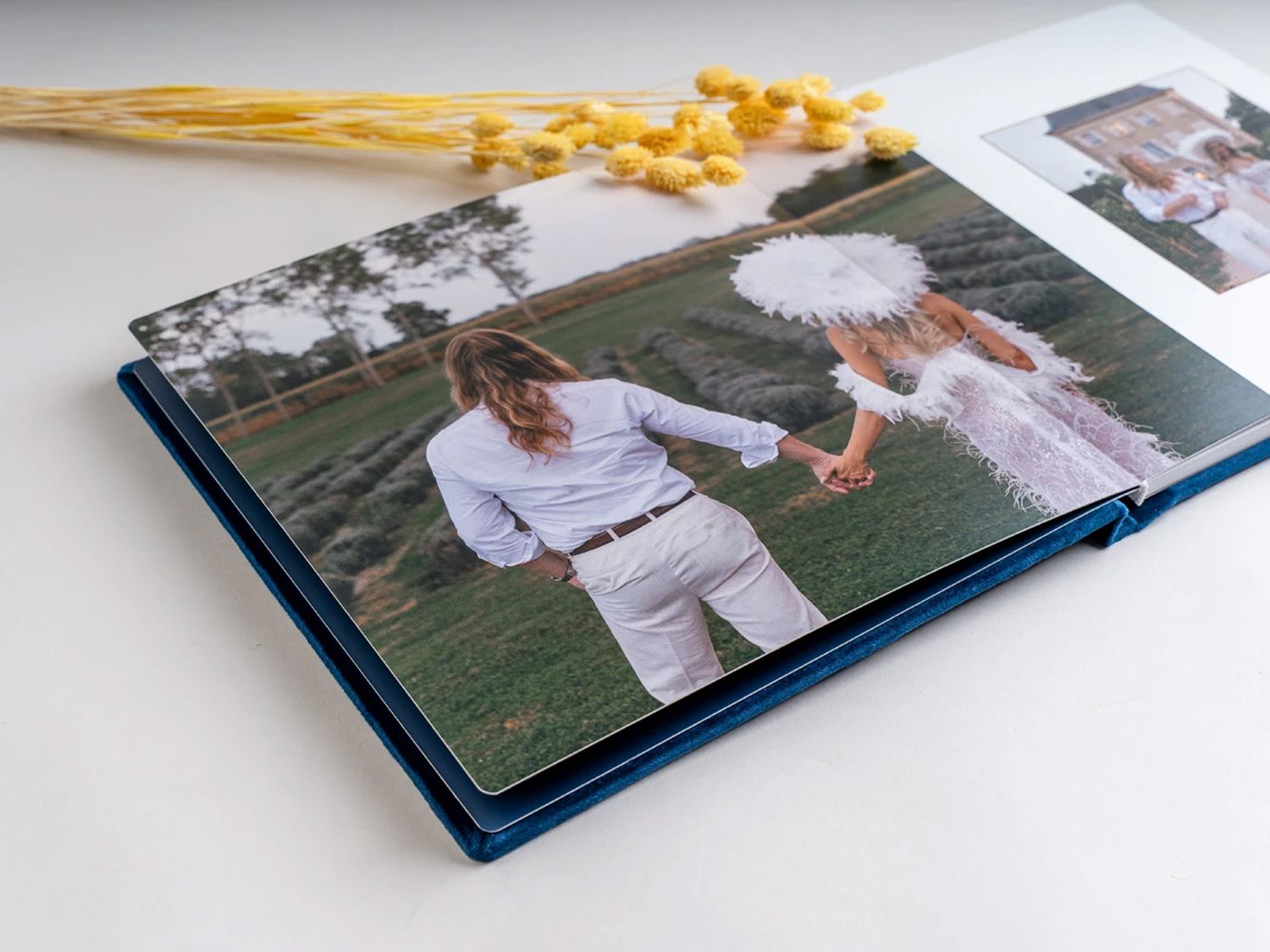 A blue hardcover photo book displaying a couple holding hands in a green field, with dried yellow flowers in the background. Northern irelan