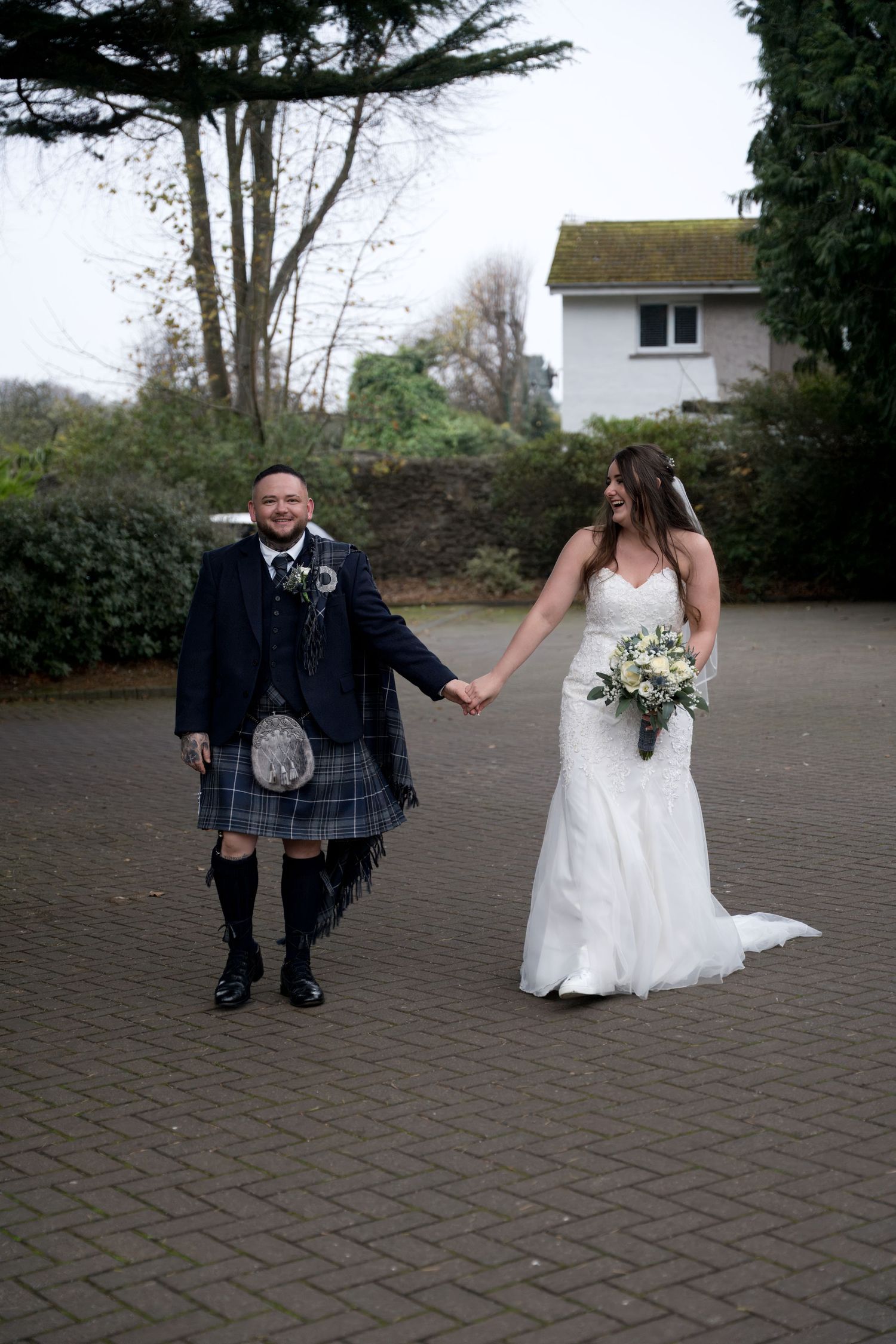 Groom in Scottish kilt holding hands with bride outdoors. Dave Martin Photographer Northern Ireland