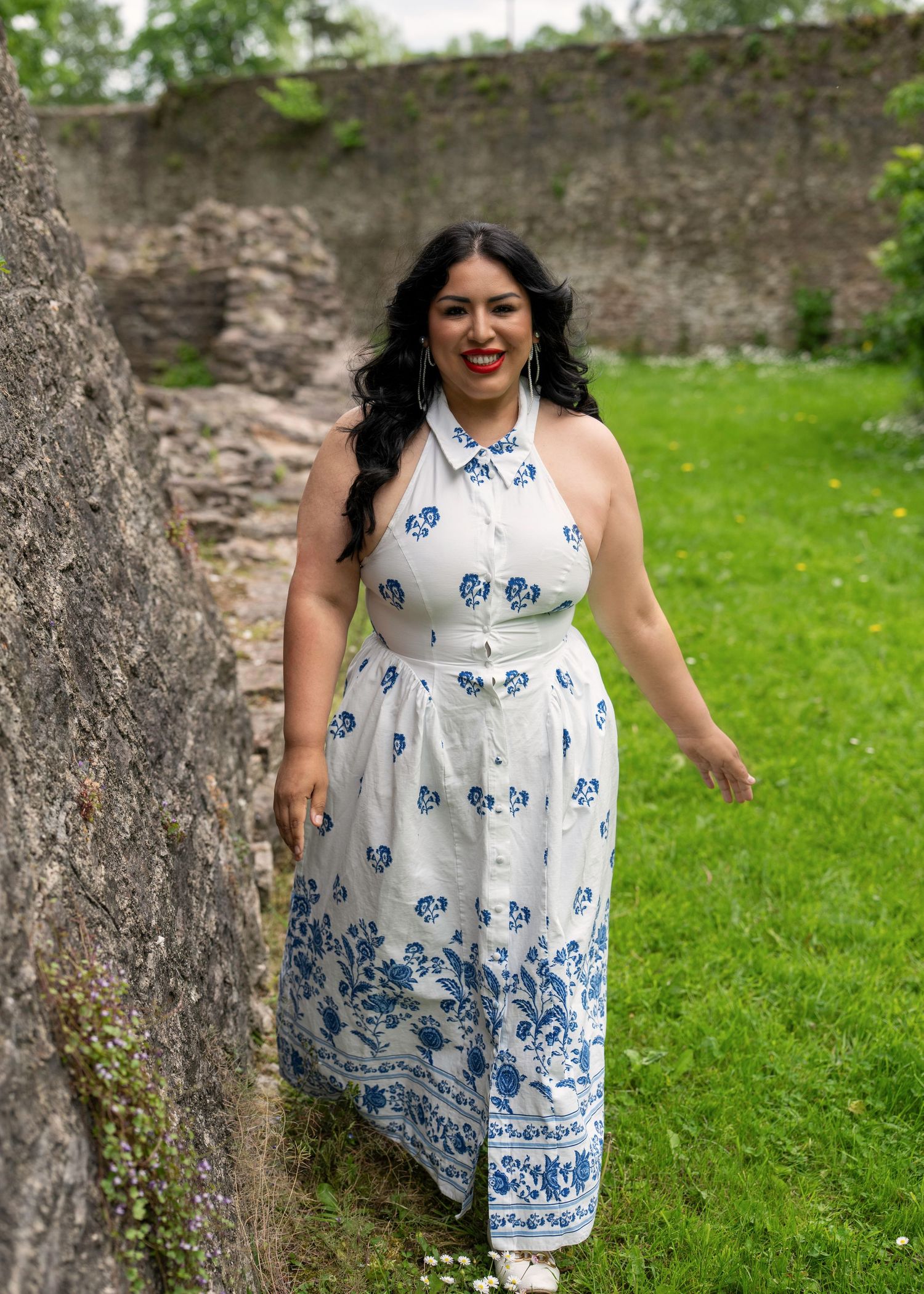 Woman in white and blue floral halter dress posing by stone wall on green lawn. Dave Martin Photography Northern Ireland
