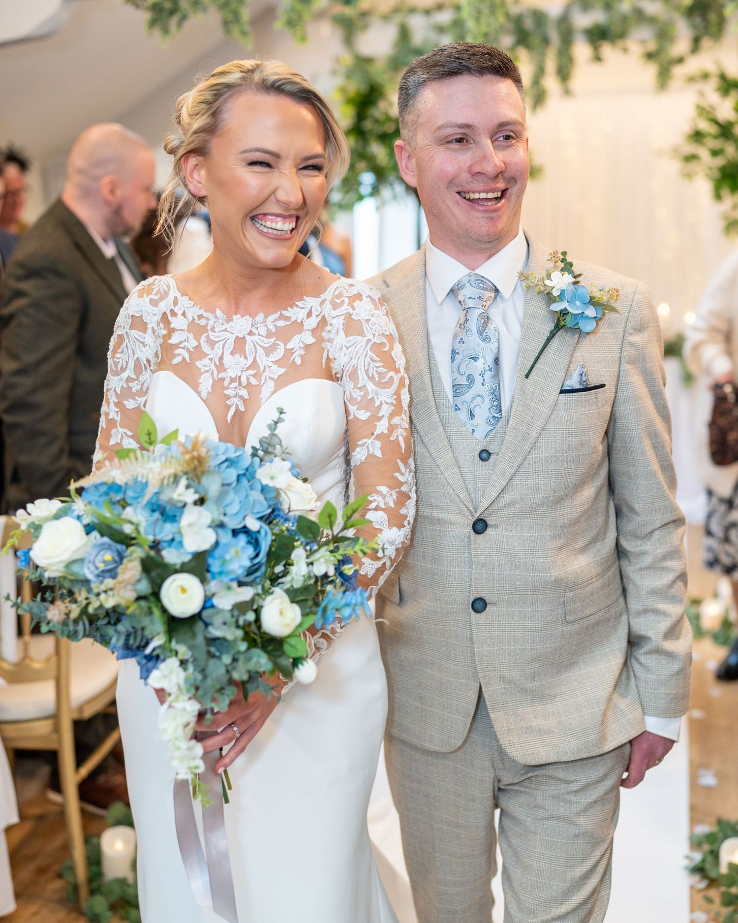 Joyful bride and groom walk down aisle laughing, bride carrying blue and white hydrangea bouquet. Dave Martin Photographer Northern Ireland