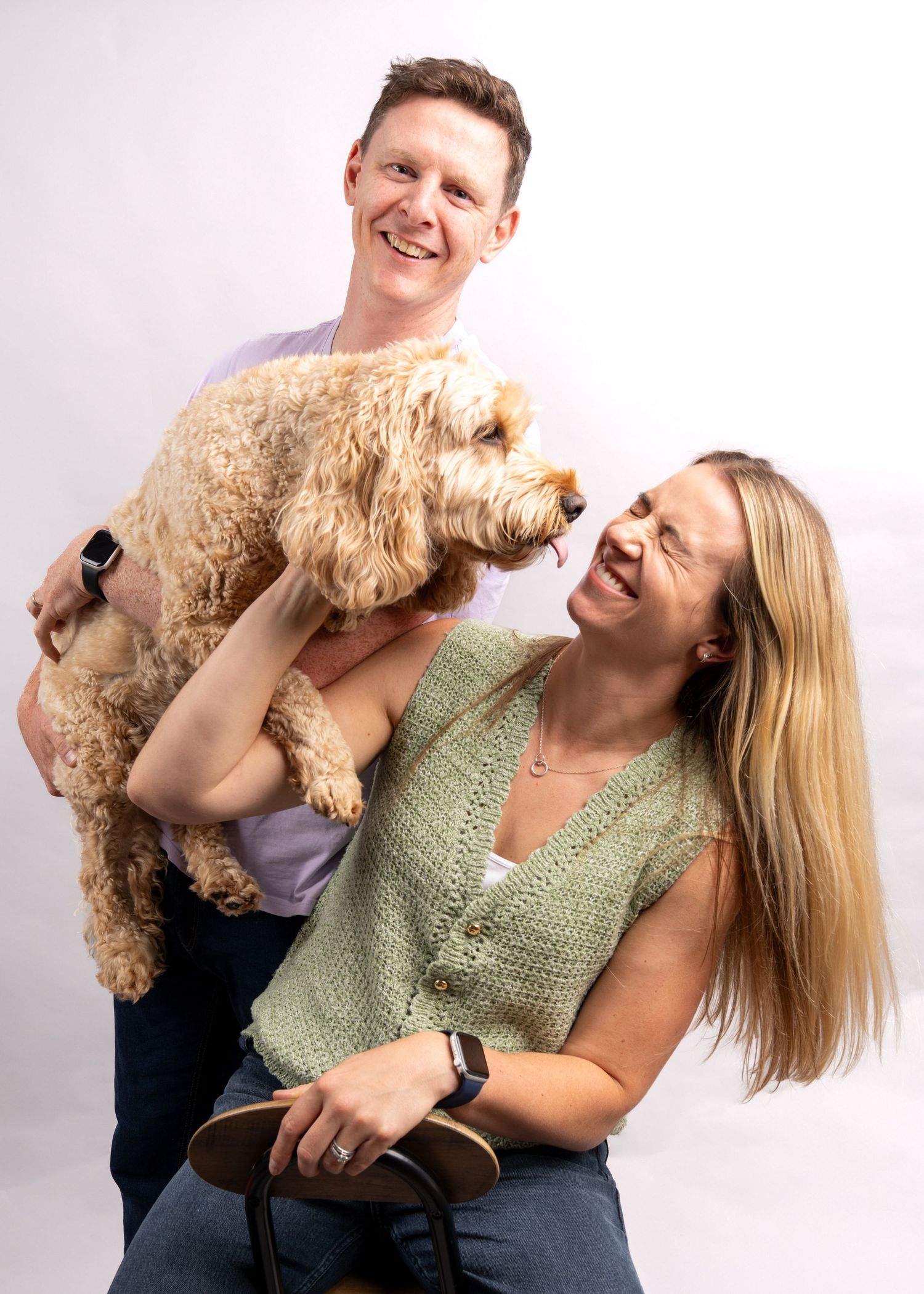 A smiling couple holding an adorable fluffy Cavoodle dog in a bright studio portrait. Dave Martin Photography Studio Belfast