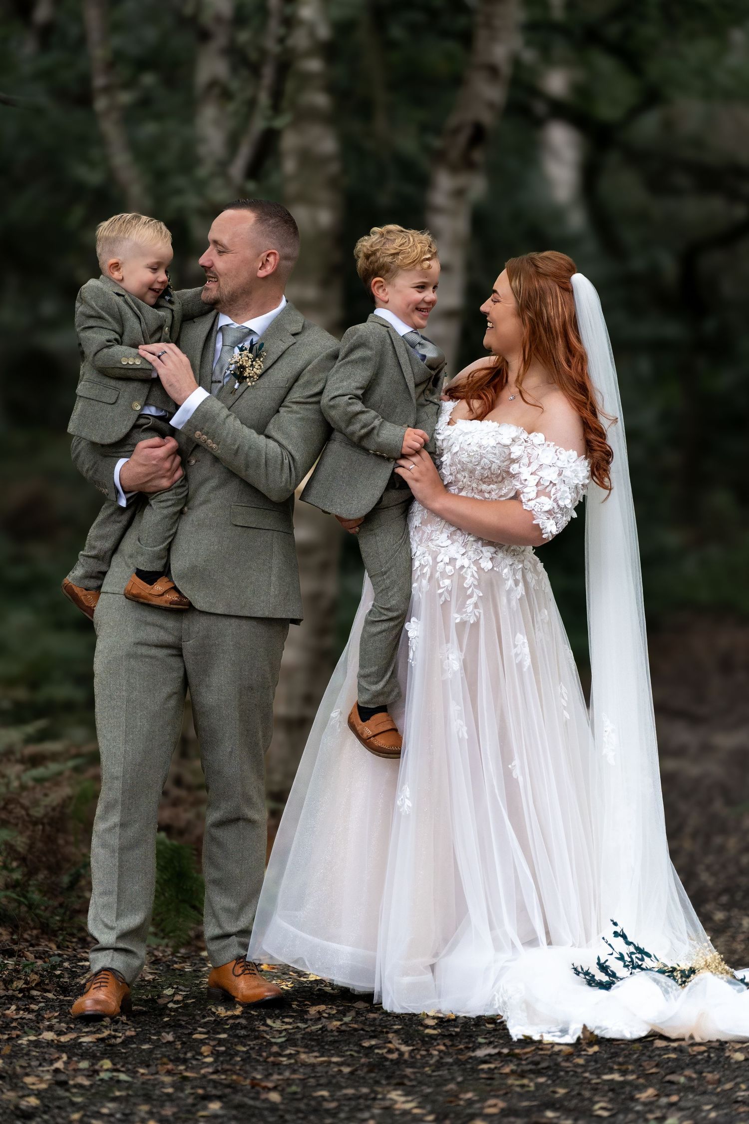 Bride and groom with two young sons in matching grey suits pose in a woodland wedding setting. Dave Martin Photographer Northern Ireland