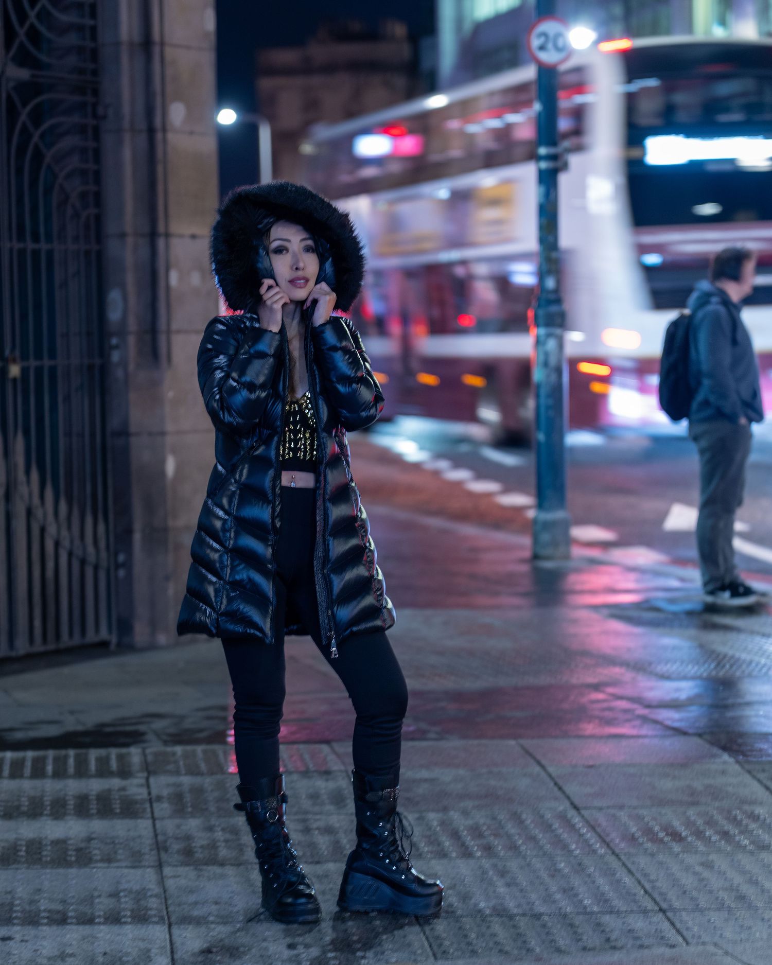 Young woman in shiny black puffer coat and platform boots posing on wet city street at night. Dave Martin celebrity Photography