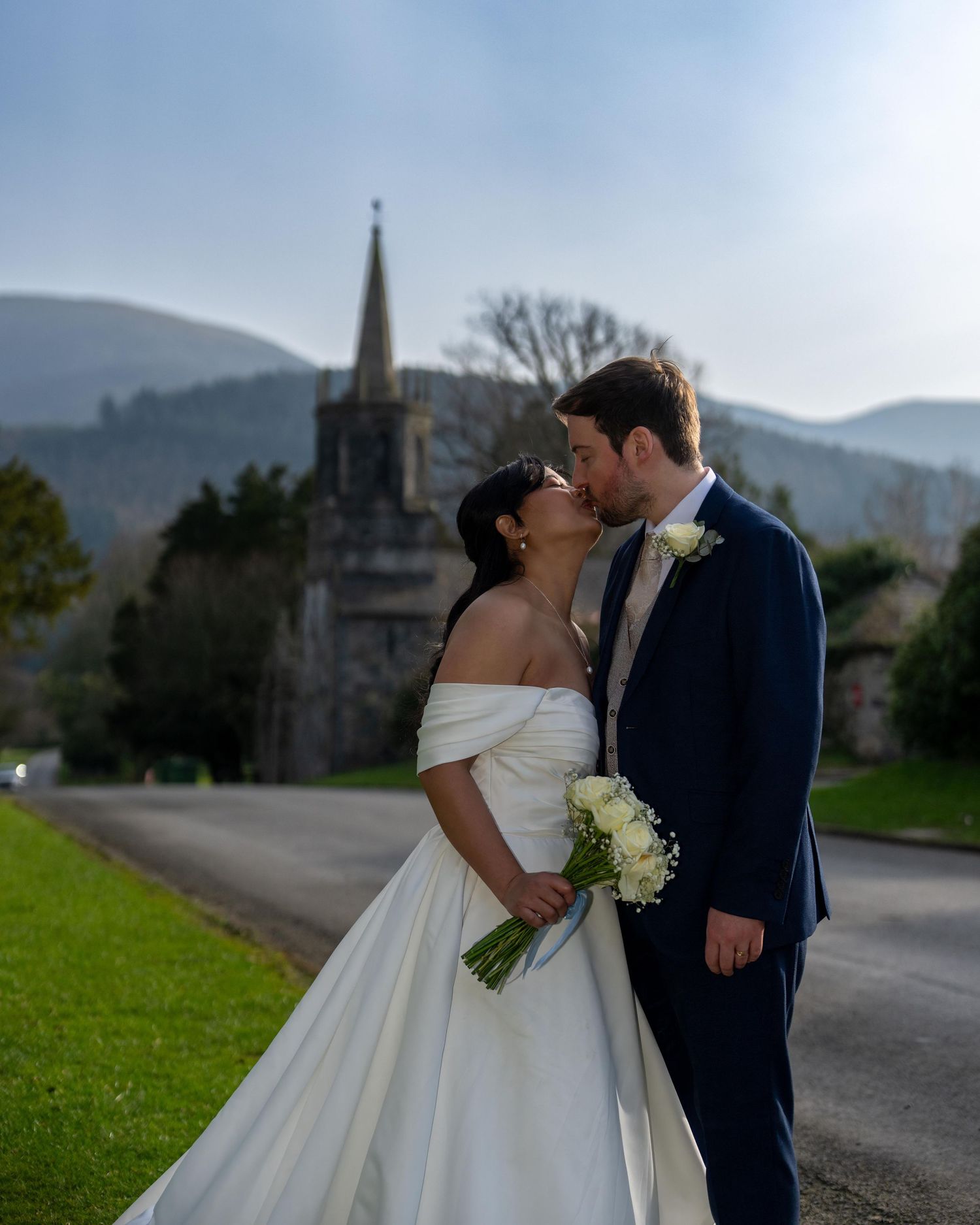 Bride and groom share a kiss outside a historic church with mountain backdrop on their wedding day.