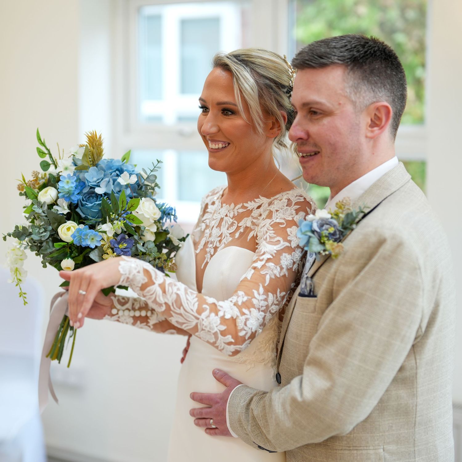 Happy bride and groom stand together during wedding ceremony, bride holding blue and white floral bouquet. Dave Martin Photographer Belfast