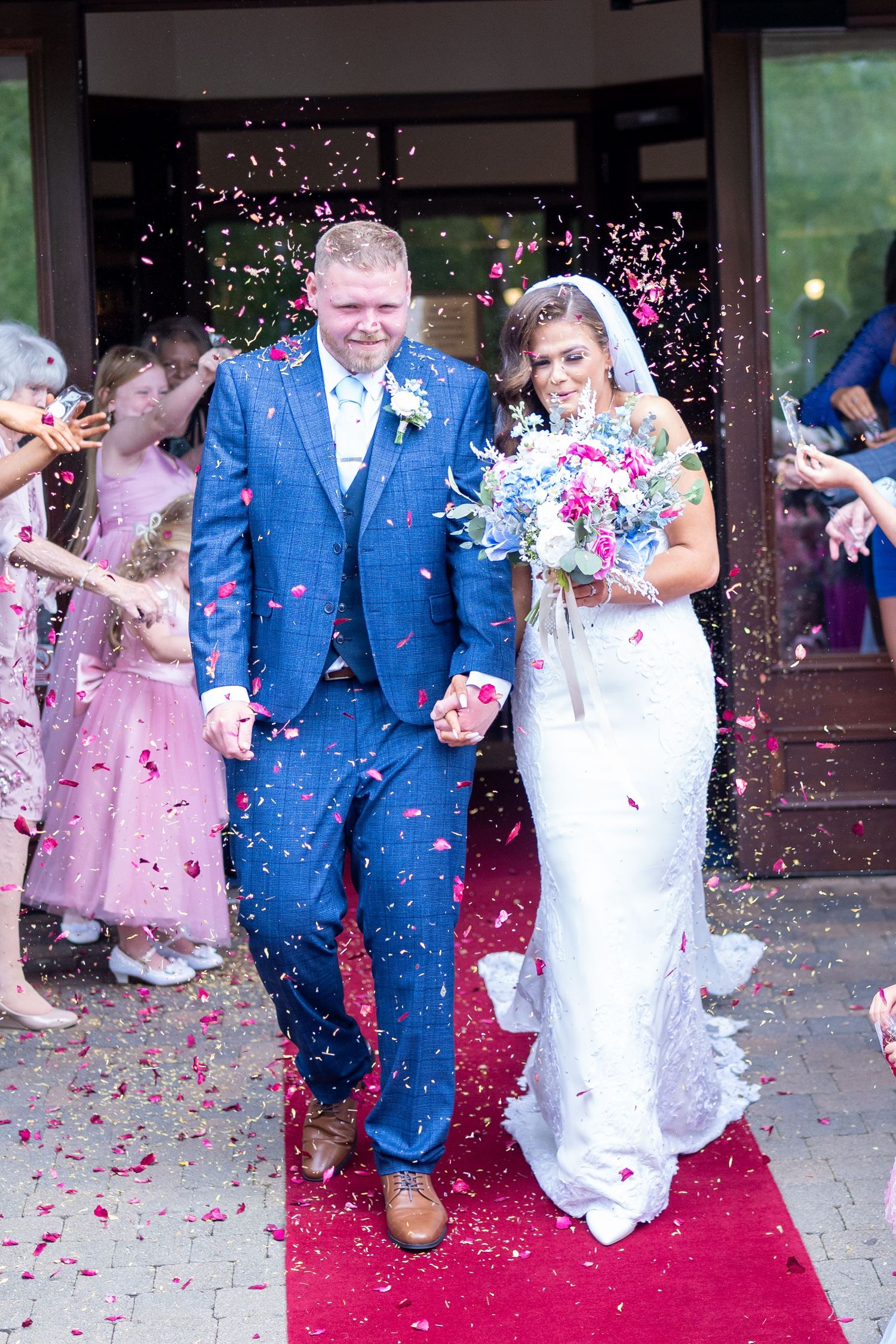 Newlyweds walking through confetti shower on red carpet after wedding ceremony. Dave Martin Photographer Northern Ireland