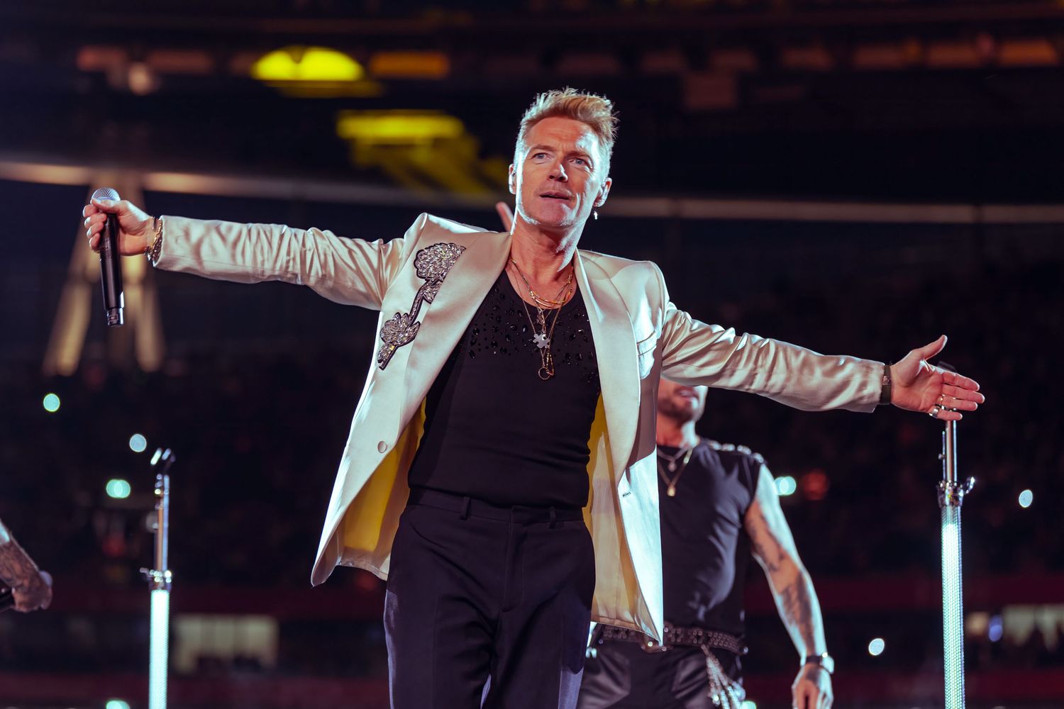 Ronan Keating in gold and white blazer performing on stage with arms outstretched holding microphone. Dave Martin celebrity Photography