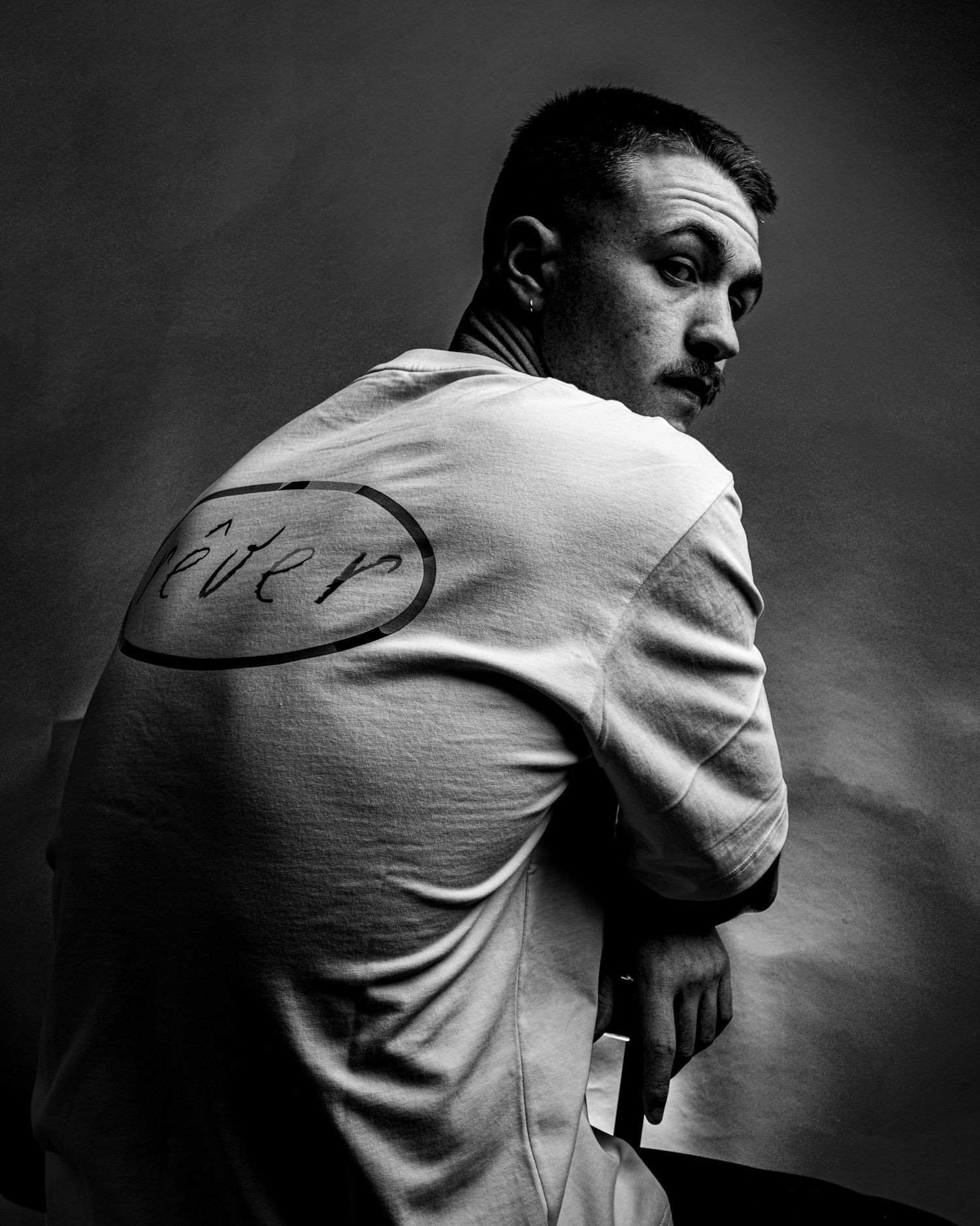 Black and white portrait of a man in a white t-shirt with text on back, looking over shoulder. Dave Martin Photography Studio Belfast