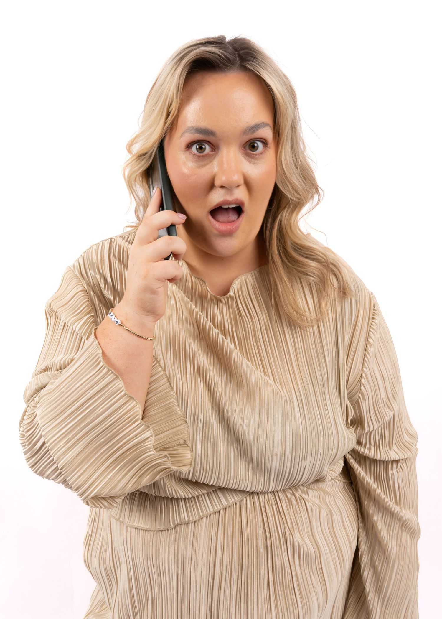 Woman in beige pleated top reacting with shock while talking on smartphone against white background. Dave Martin Photography Studio Belfast
