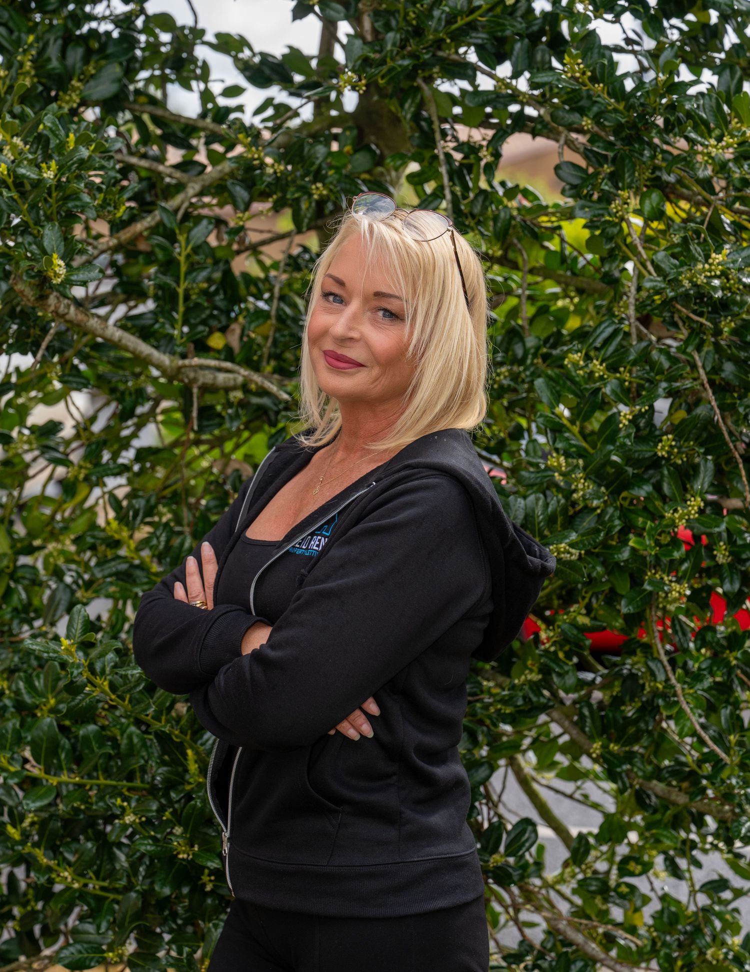Blonde woman in black hoodie posing with arms crossed in front of green foliage. Dave Martin Photography Northern Ireland