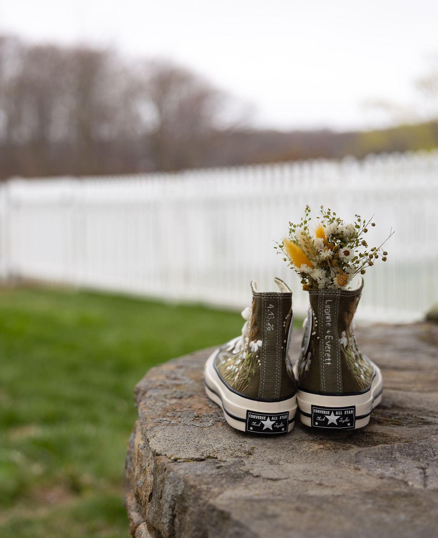 Olive green Converse high-top sneakers filled with dried wildflowers displayed on a stone outdoors.