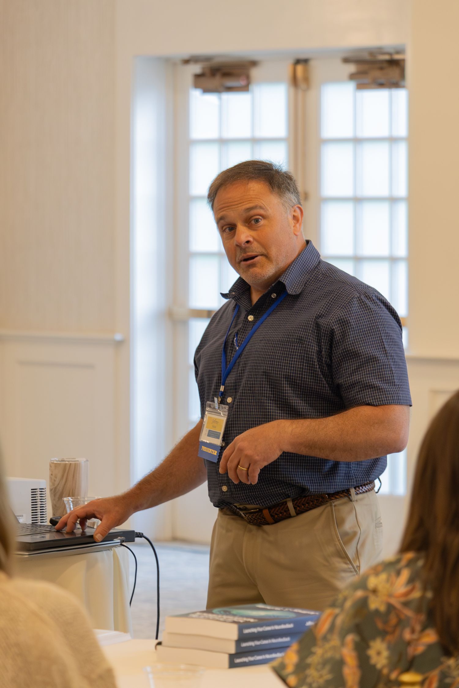 Man in blue polo shirt presenting at a conference session while standing at a table.