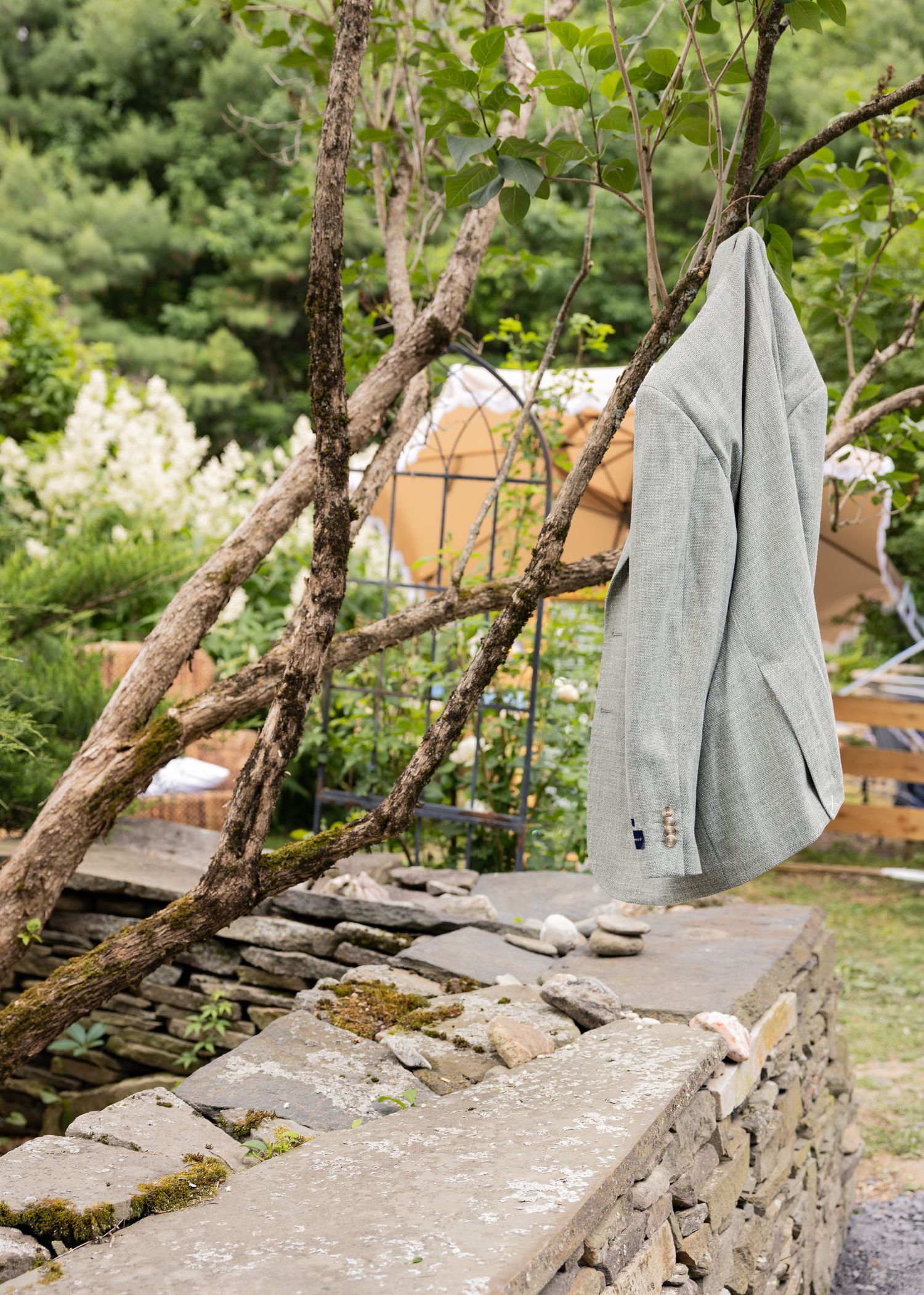 Gray linen jacket hanging on tree branches over stone wall with glamping dome in background.