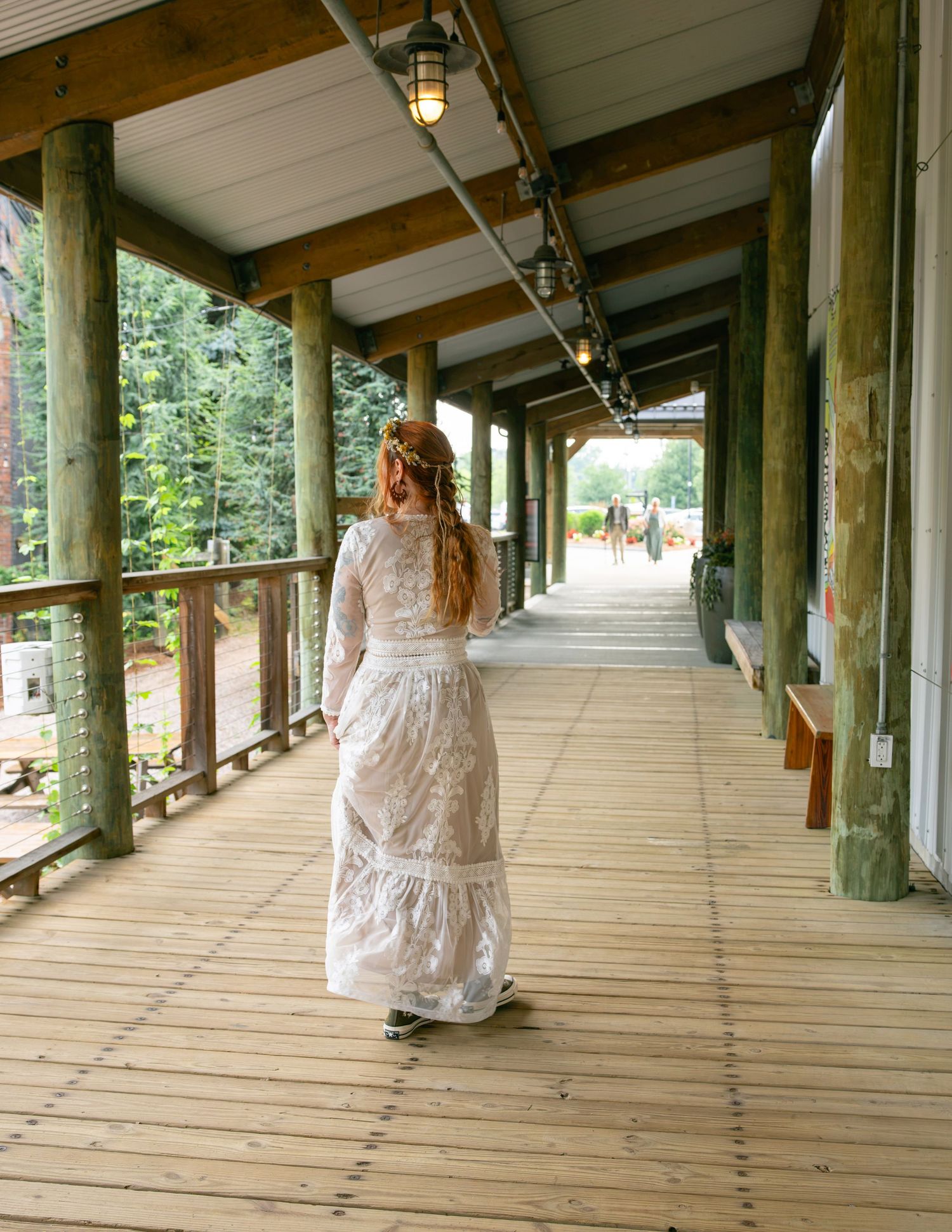 Bride in lace boho wedding dress with long red hair walks along rustic wooden covered porch outdoors.