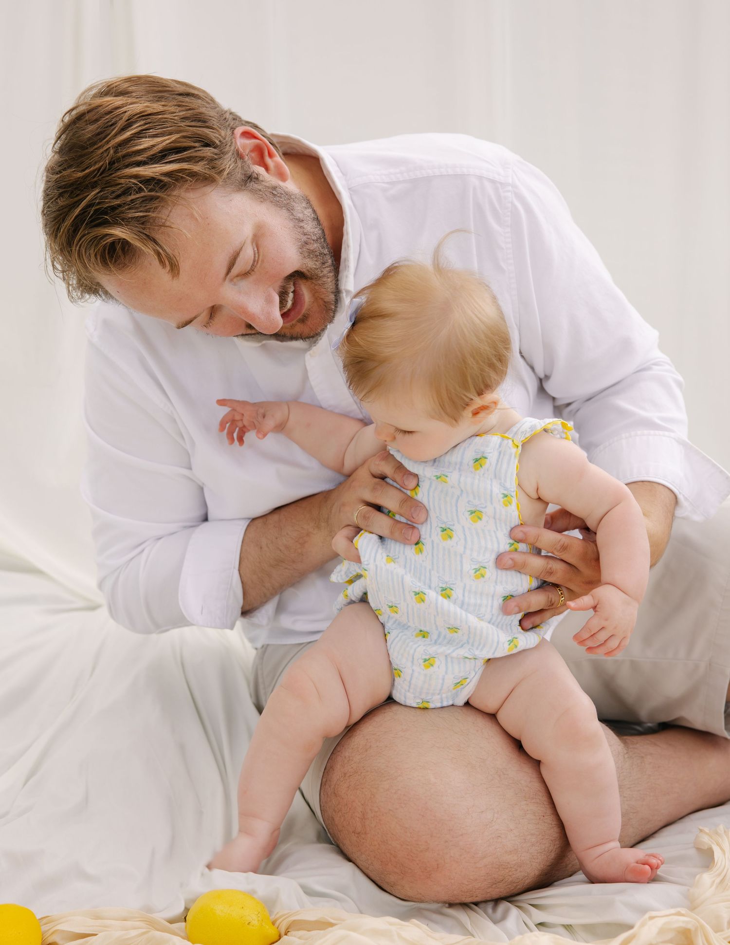 Bearded father smiling warmly while holding his baby in a lemon-print onesie during a photo session.