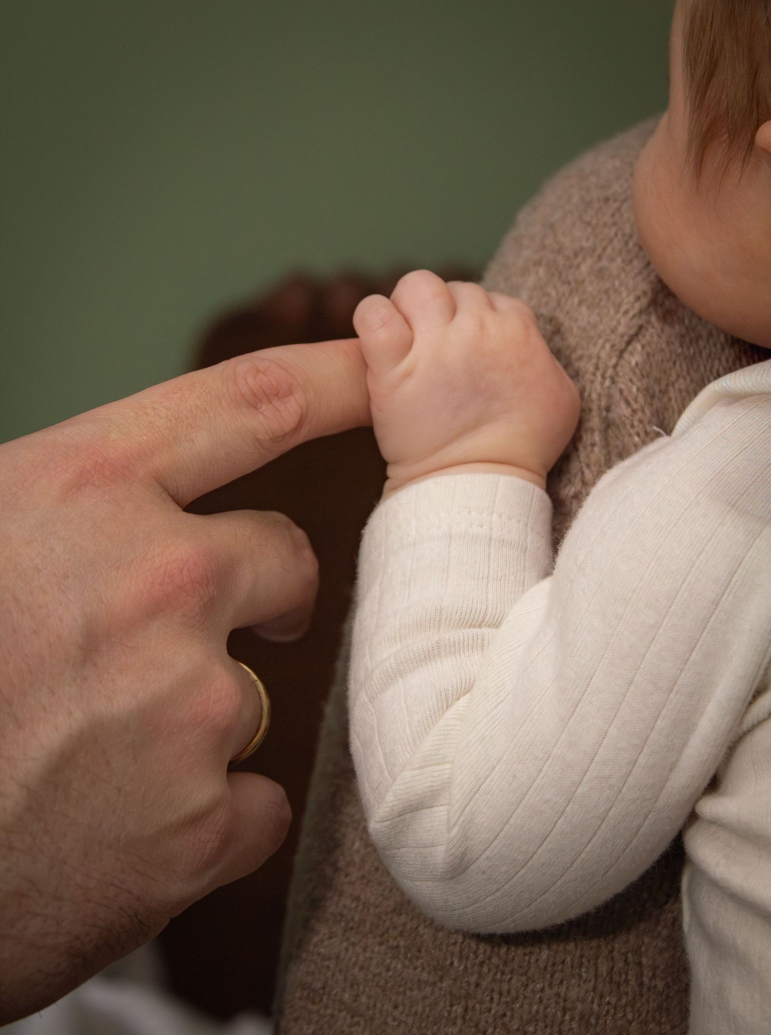 Newborn baby gripping fathers finger while being held against a parents chest indoors.