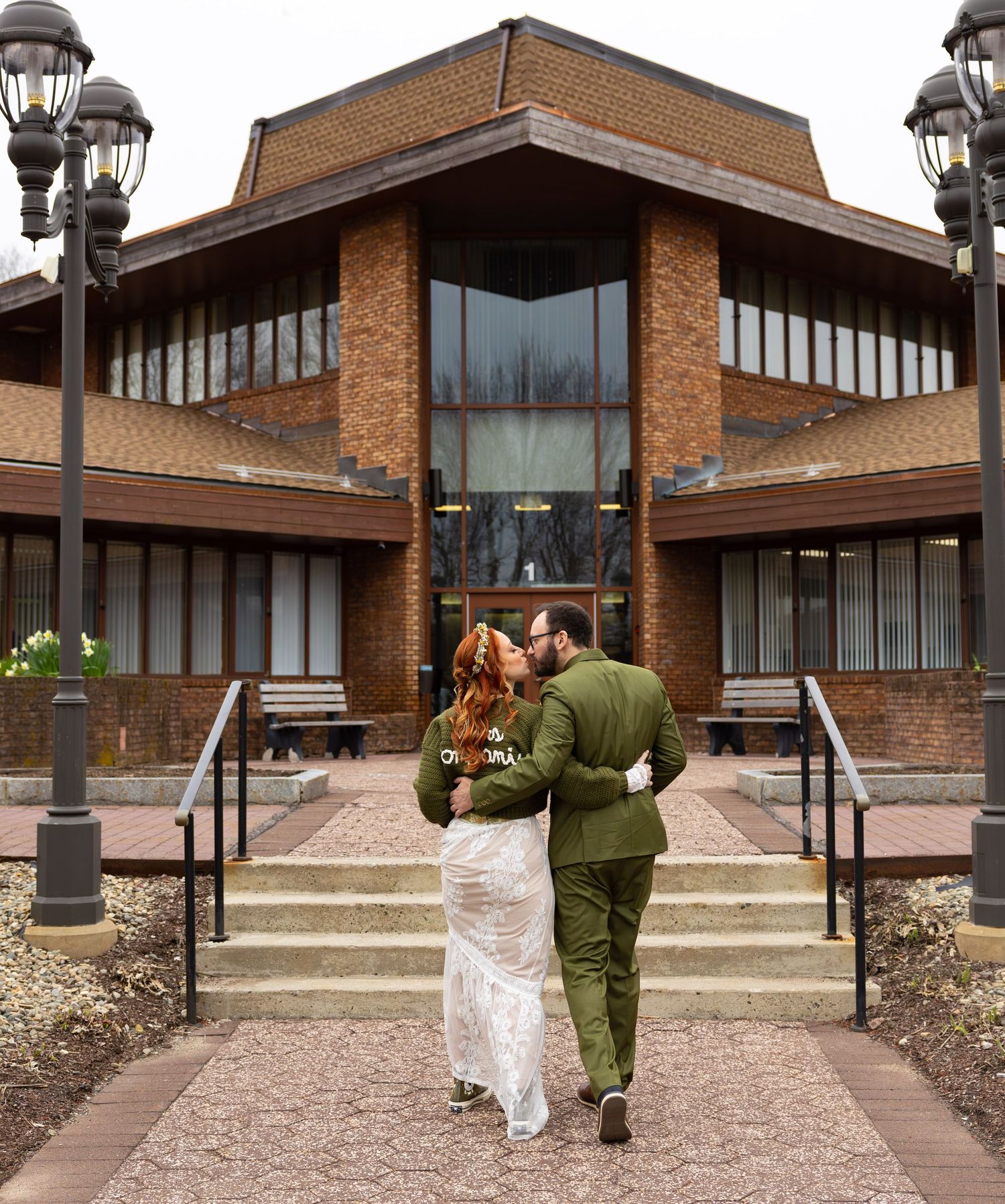 Newlywed couple kissing on steps outside brick building in wedding attire.