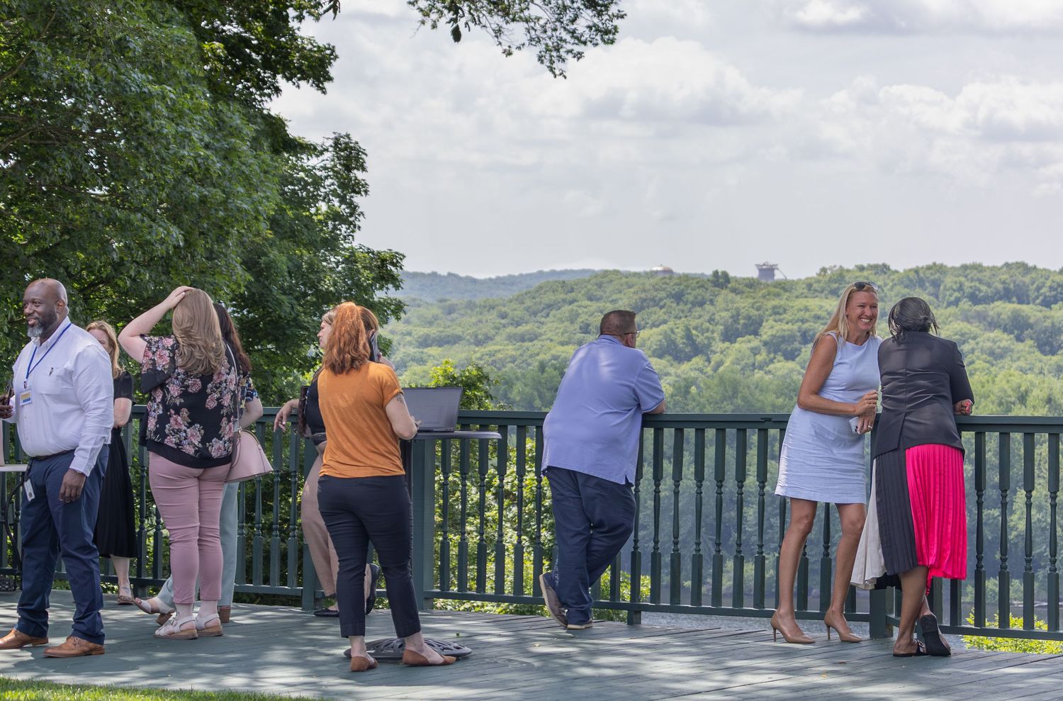 Group of people networking on an outdoor deck overlooking a lush green valley landscape.