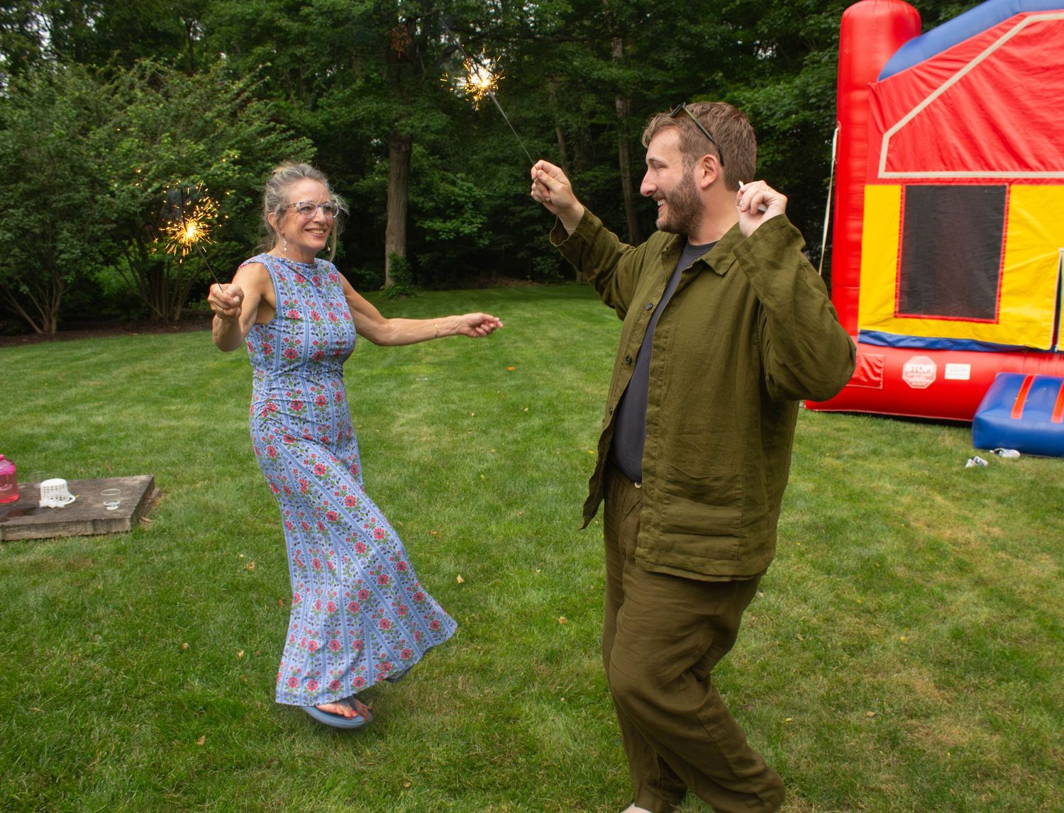 Couple celebrating outdoors with sparklers near a bounce house on a green lawn at dusk.