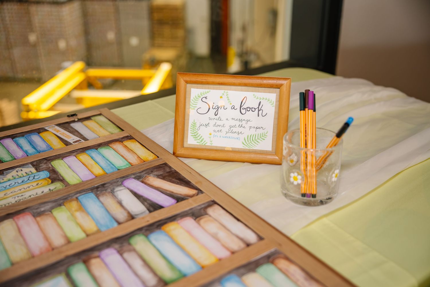 Wedding guest book signing station with colorful chalk pastels, markers, and framed sign on table.