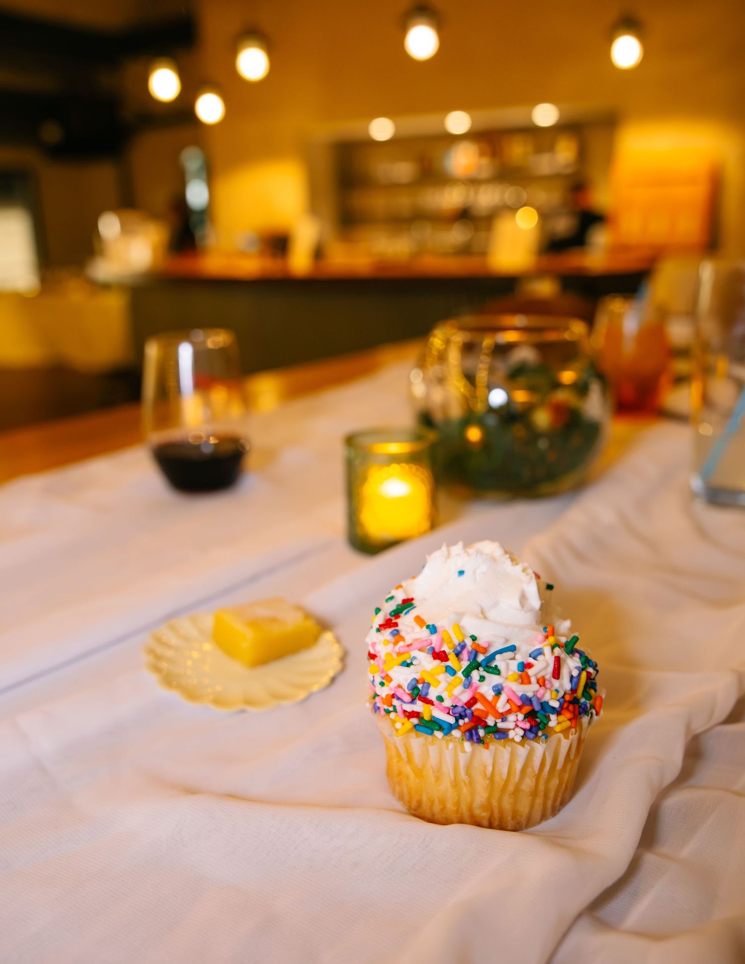 Colorful sprinkle cupcake with whipped frosting on white tablecloth at wedding reception dinner table.