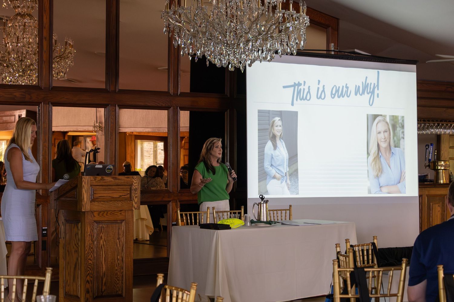 Two women present at elegant event venue with This Is Our Why projection screen displayed.