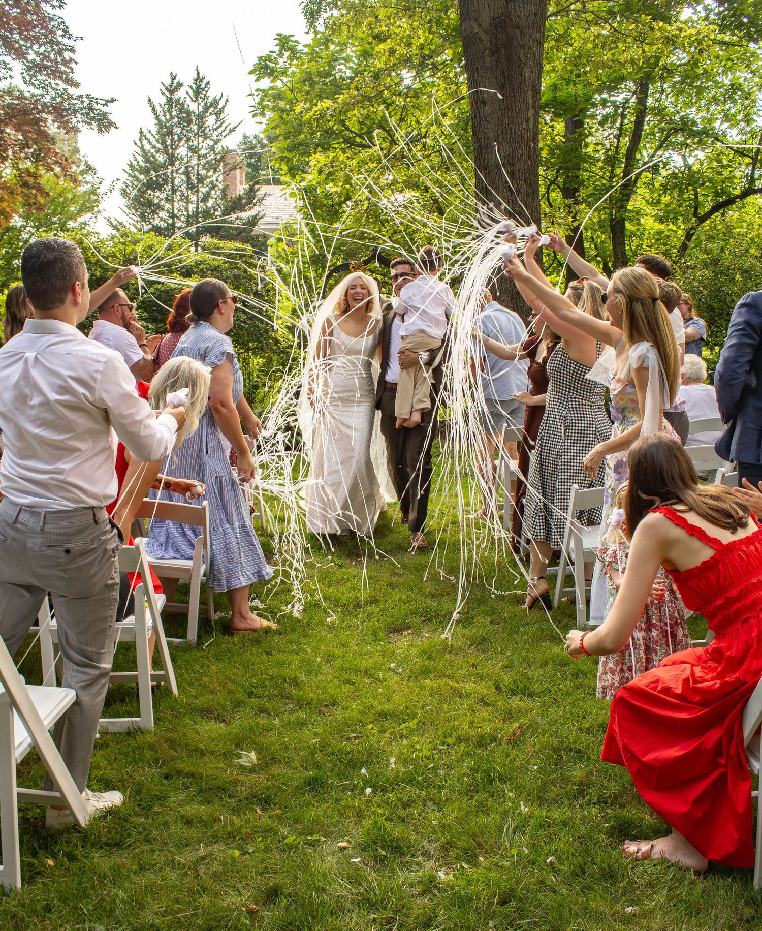 Wedding guests toss white streamers over bride and groom during joyful outdoor ceremony exit.