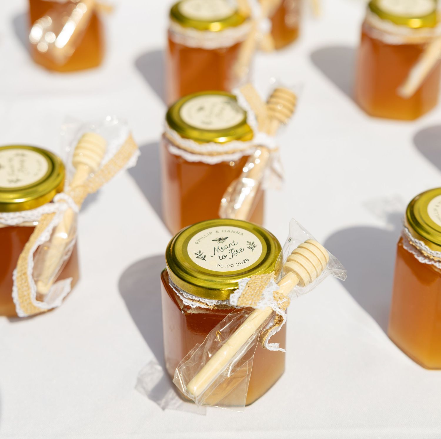 Small glass jars of honey with wooden dippers and lace ribbon bows arranged as elegant wedding favor gifts.