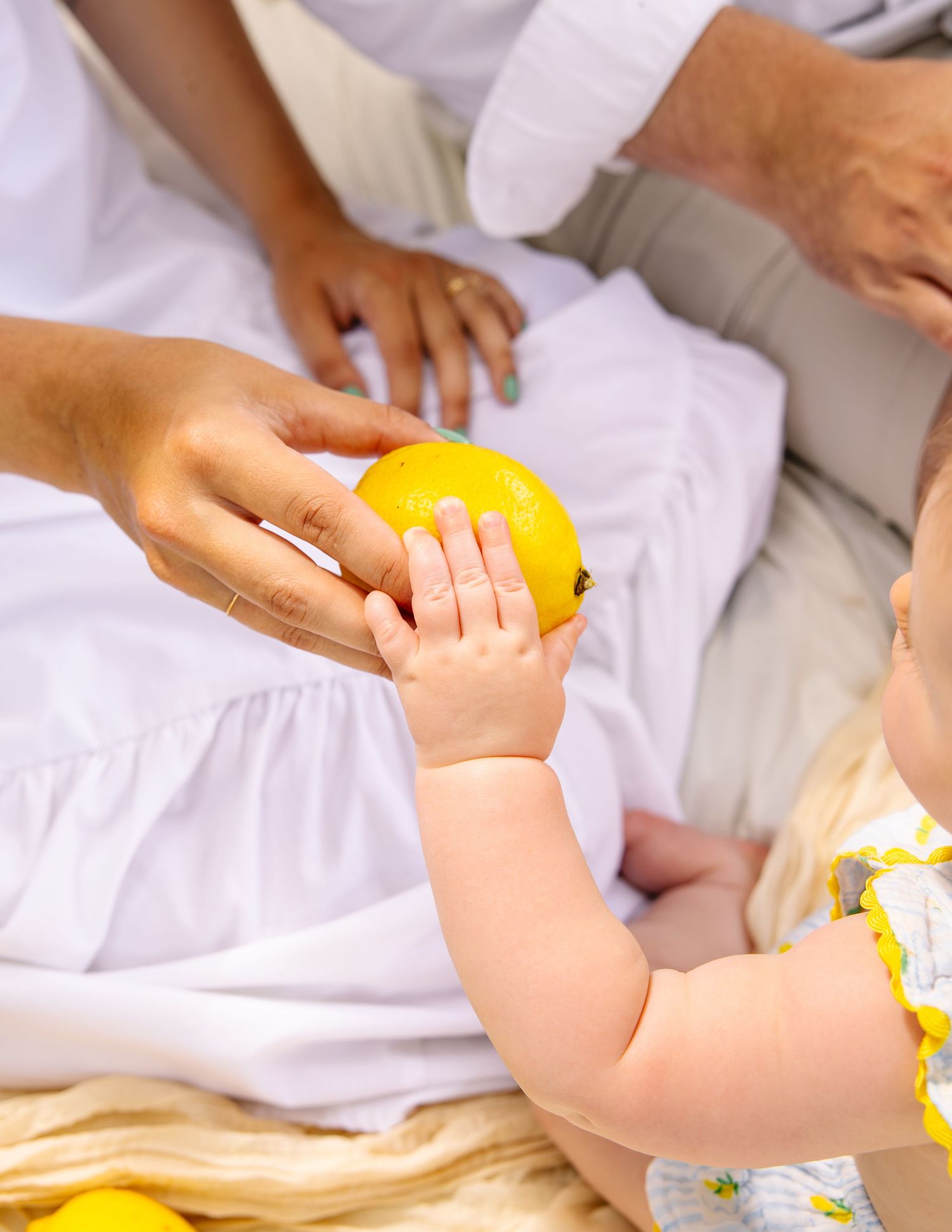Close-up of adult hand offering a bright yellow lemon to a curious baby.