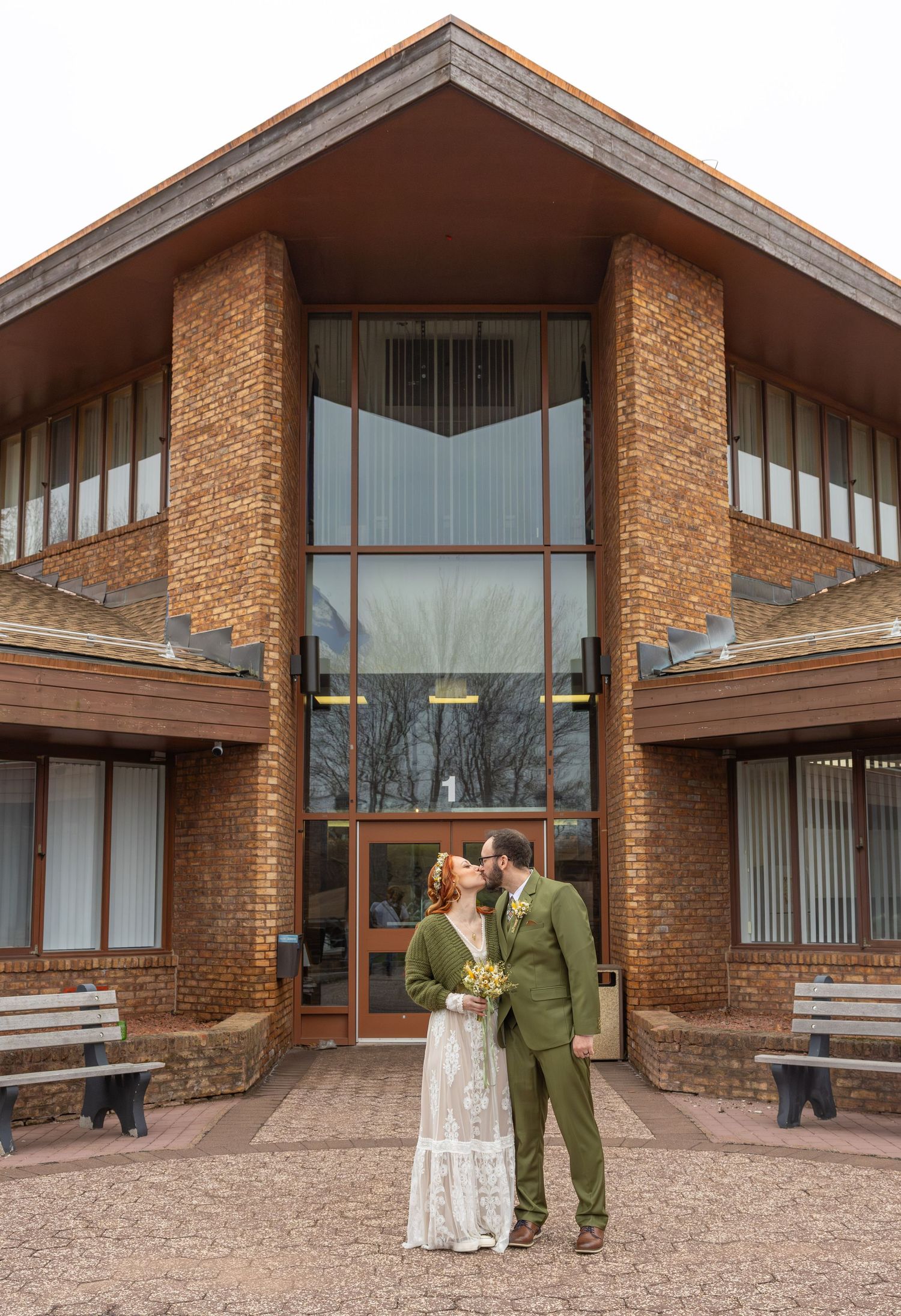 Newlywed couple kissing in front of modern brick building after courthouse wedding ceremony.