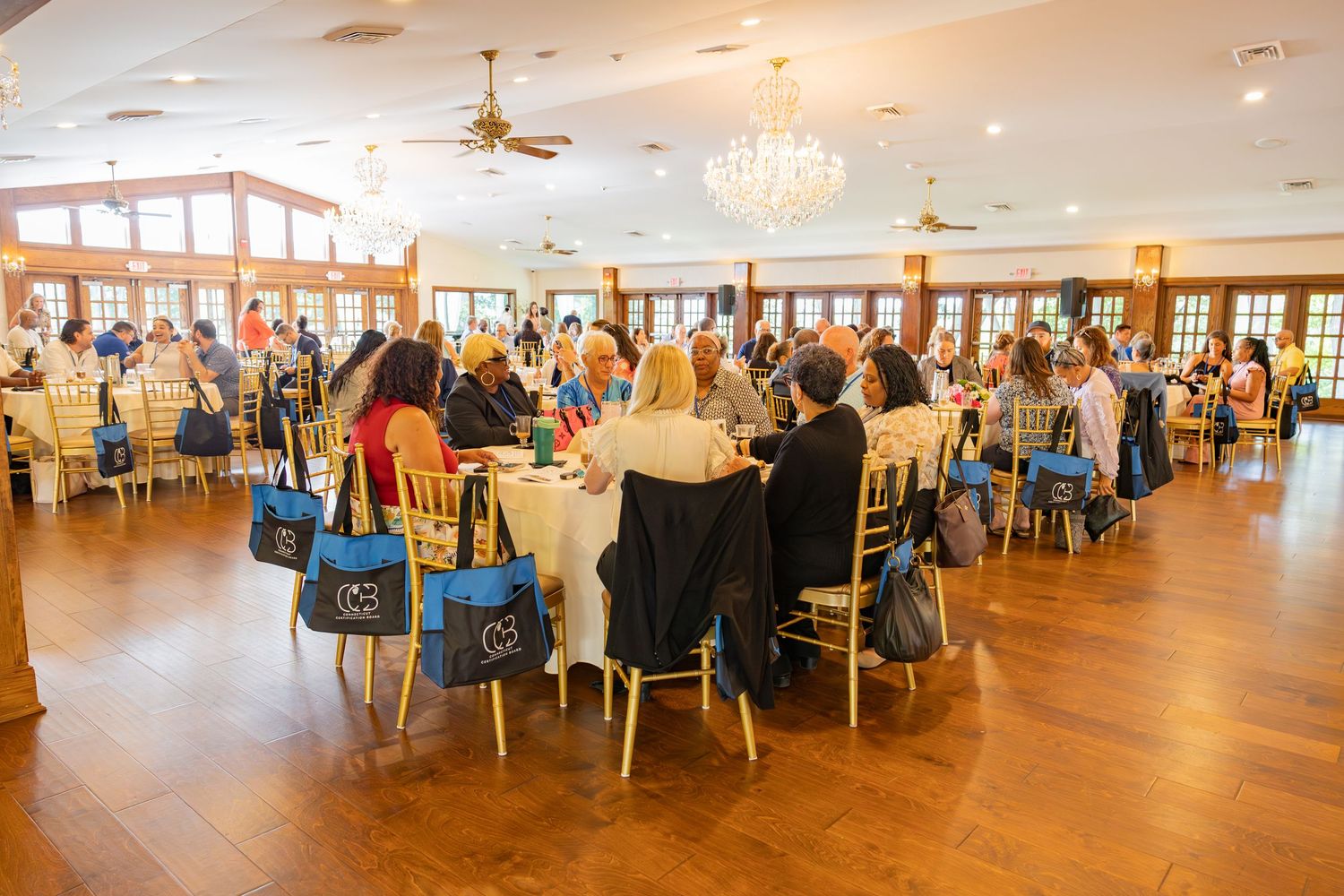 Large professional conference gathering with attendees seated at round tables in bright elegant ballroom venue.
