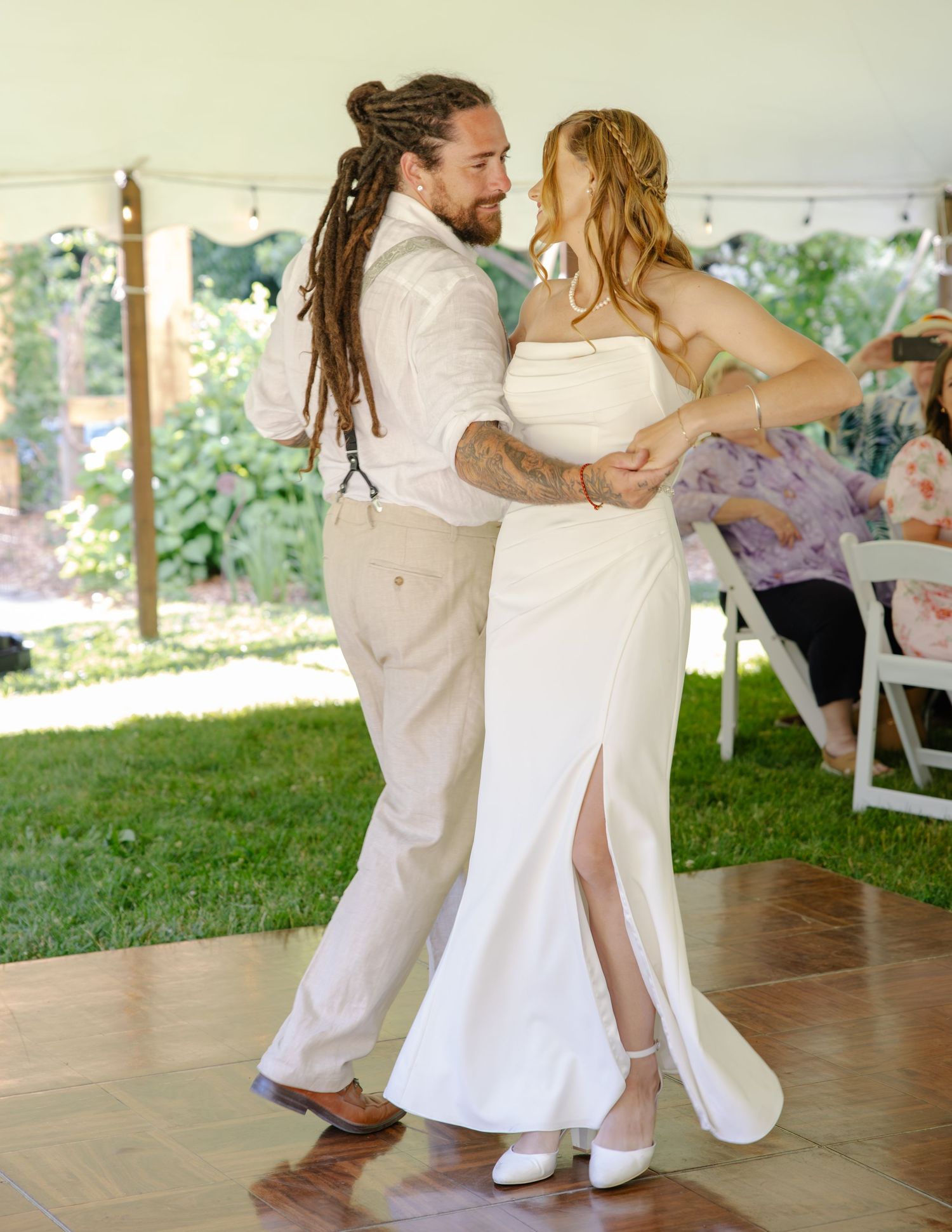 Newlywed couple sharing their first dance under a white tent at an outdoor wedding reception.